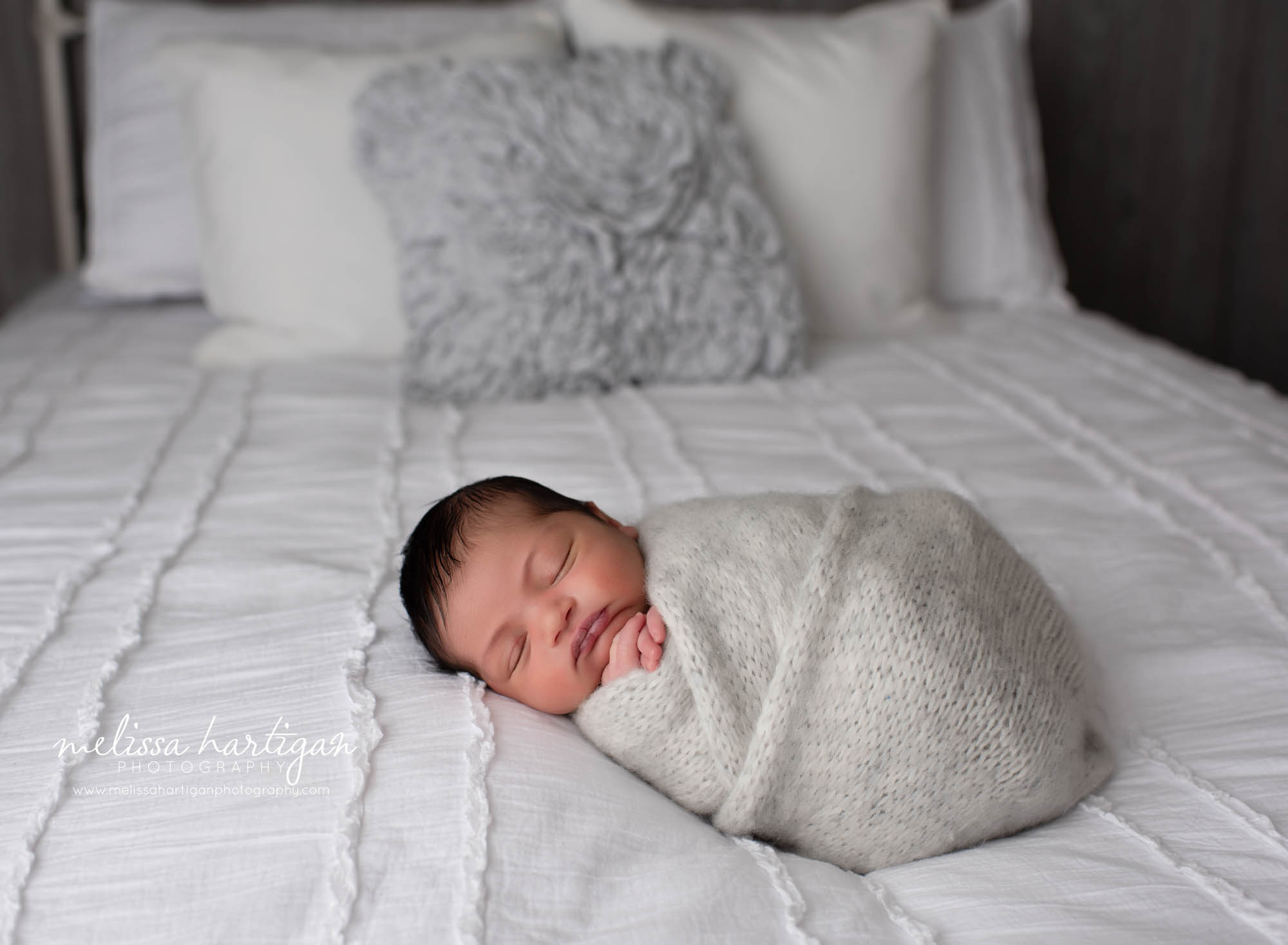 newborn baby boy posed on bed in knitted light gray wrap