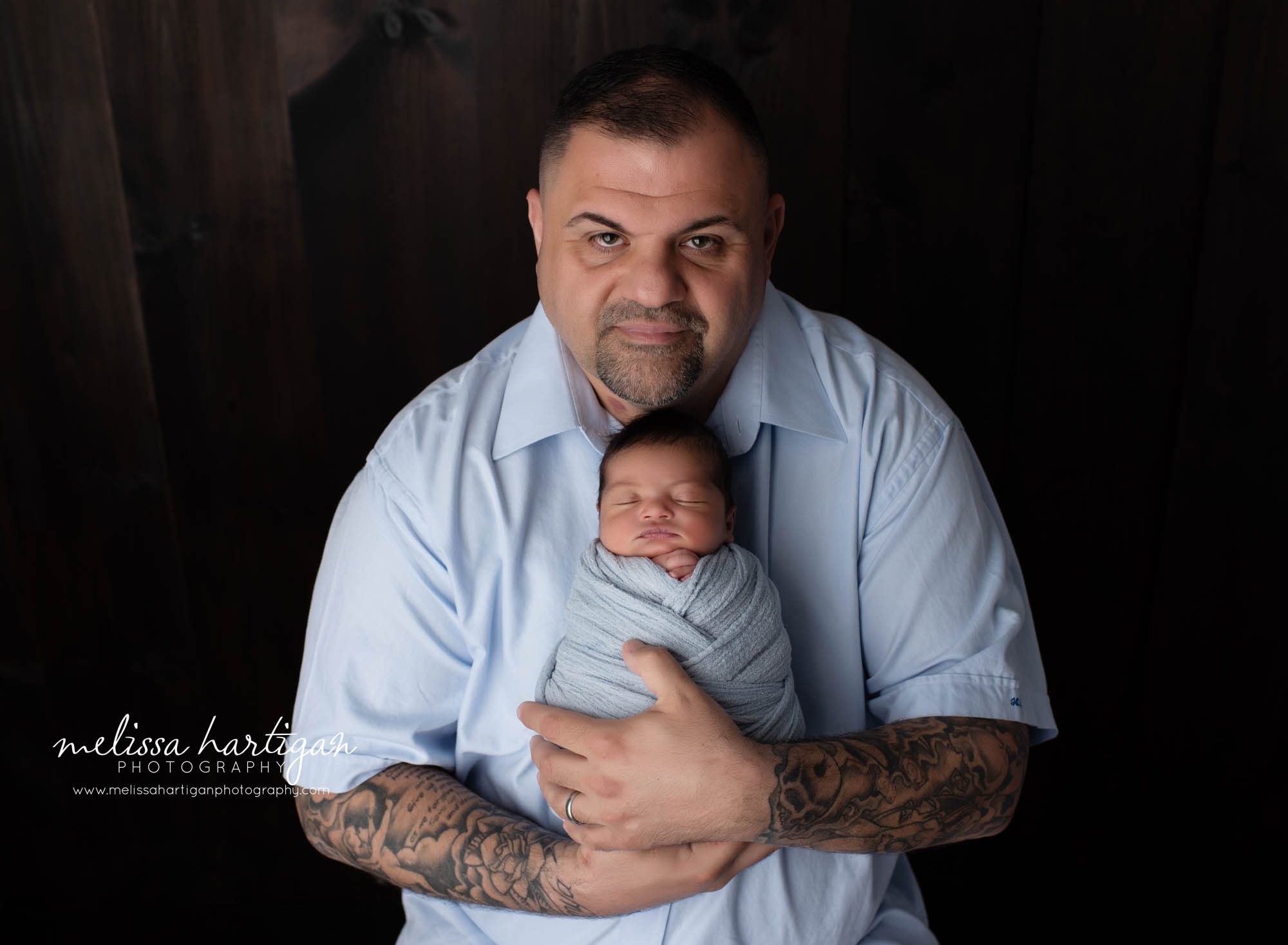 dad holding newborn son all wrapped in blue wrap