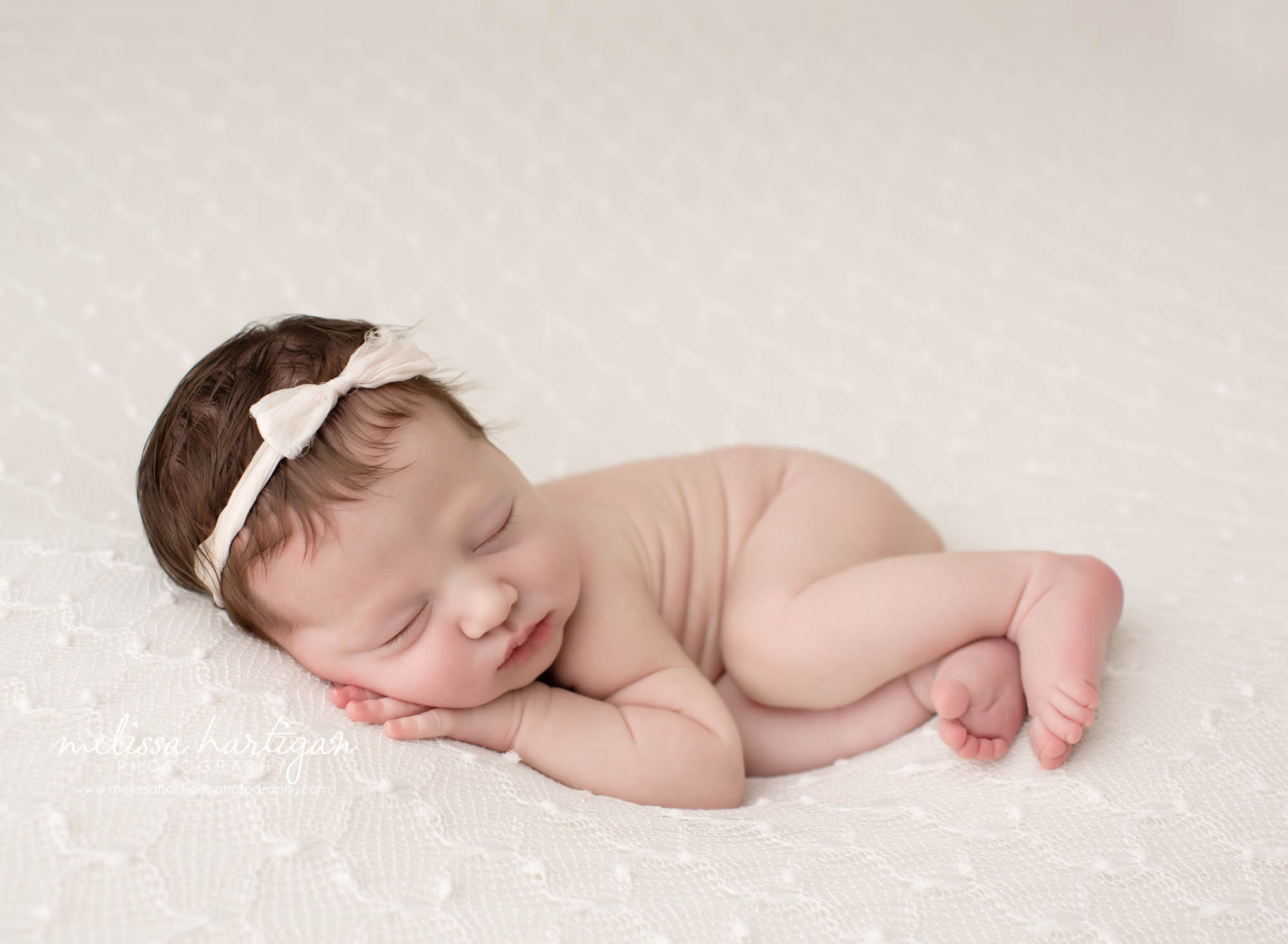 Baby girl posed on side with cream bow headband on cream textured backdrop