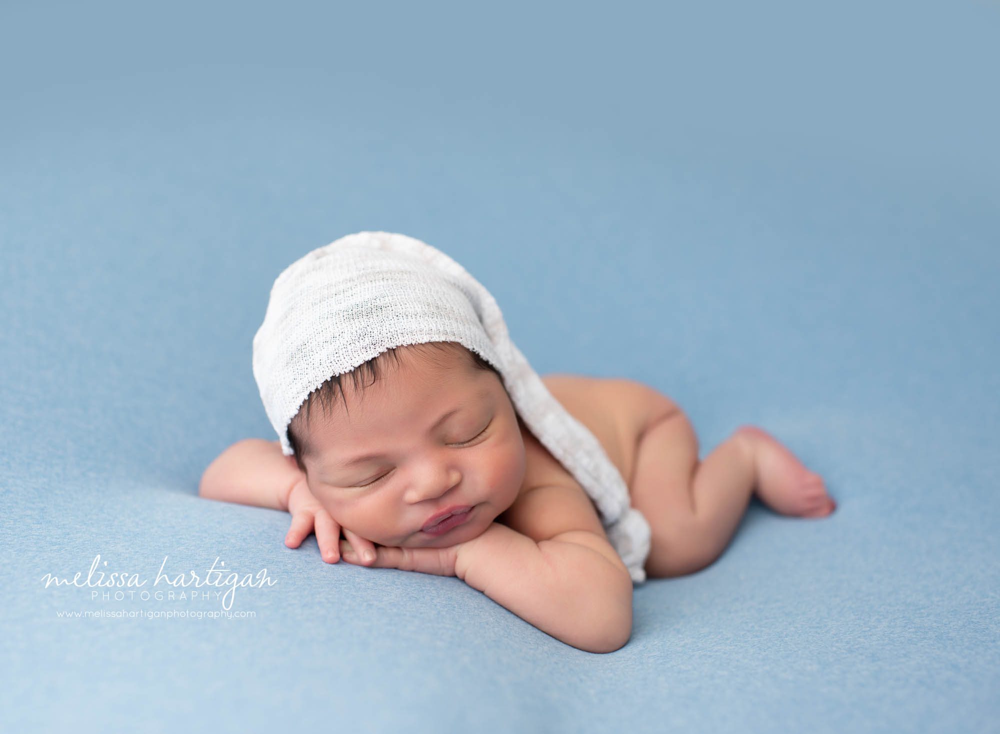 Baby boy posed on blue backdrop with cream sleepy cap and sleeping in adorable pose