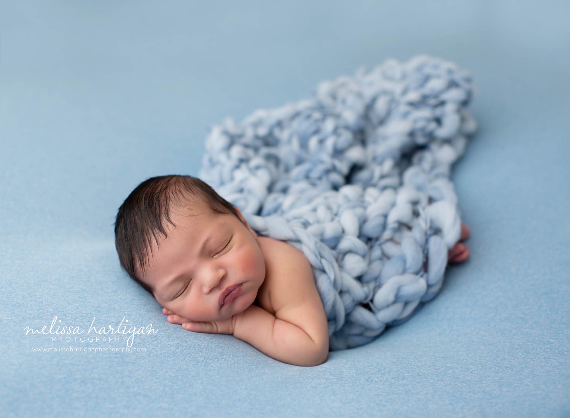 Baby boy posed on side with knitted chunky blanket