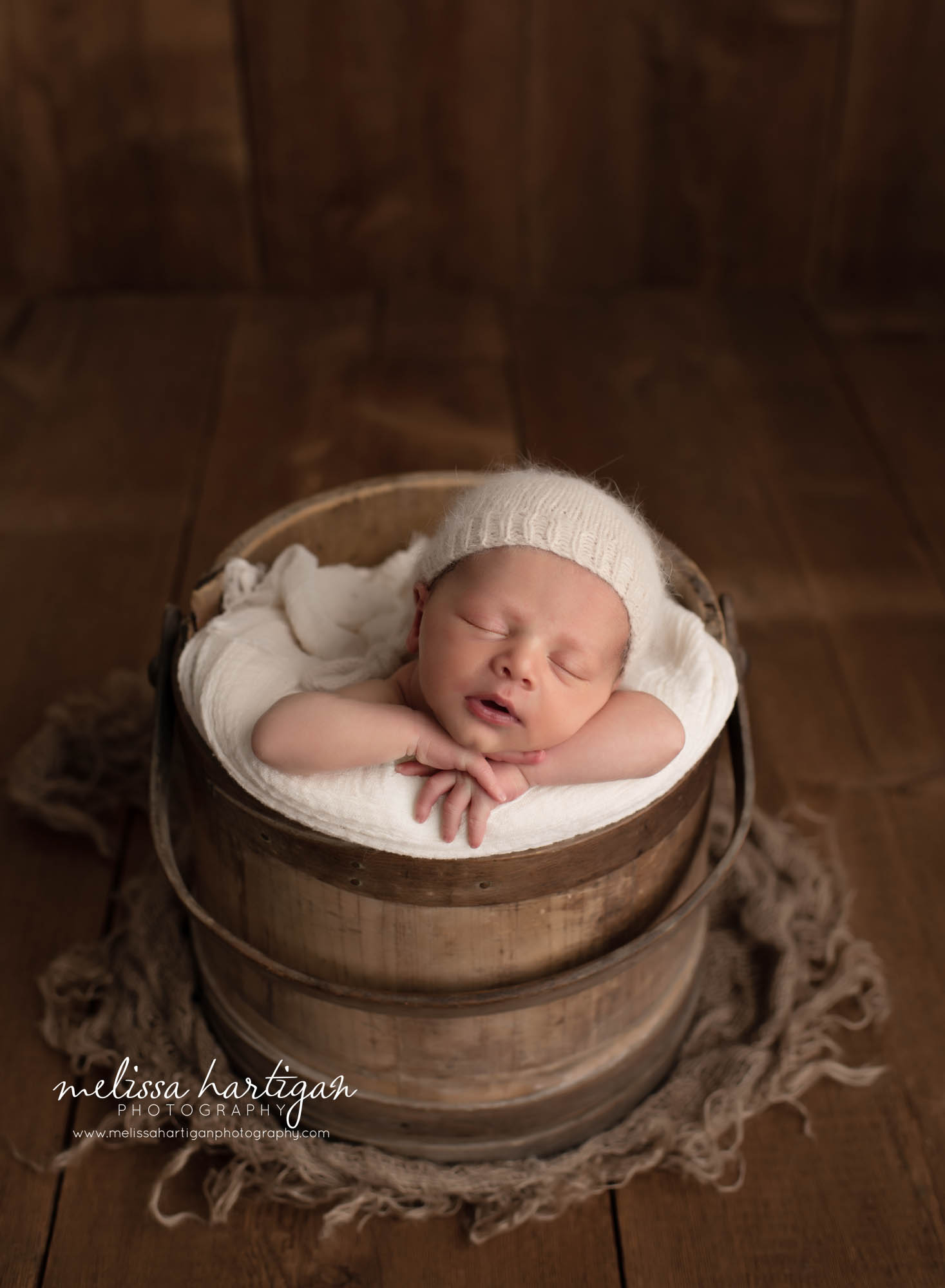 Baby posed in bucket with cream layer and knitted sleepy cap
