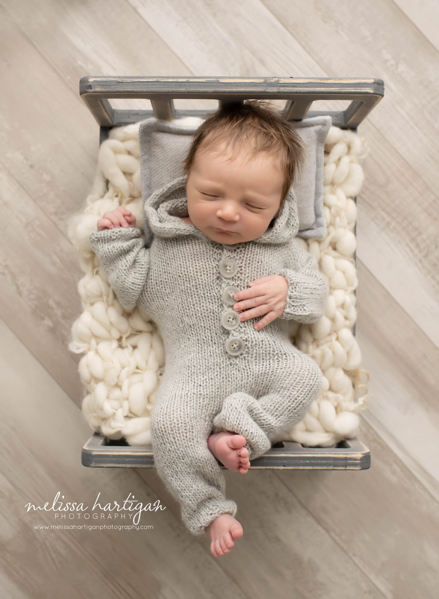 Newborn baby boy posed on wooden bed laying on back wearing grey outfit