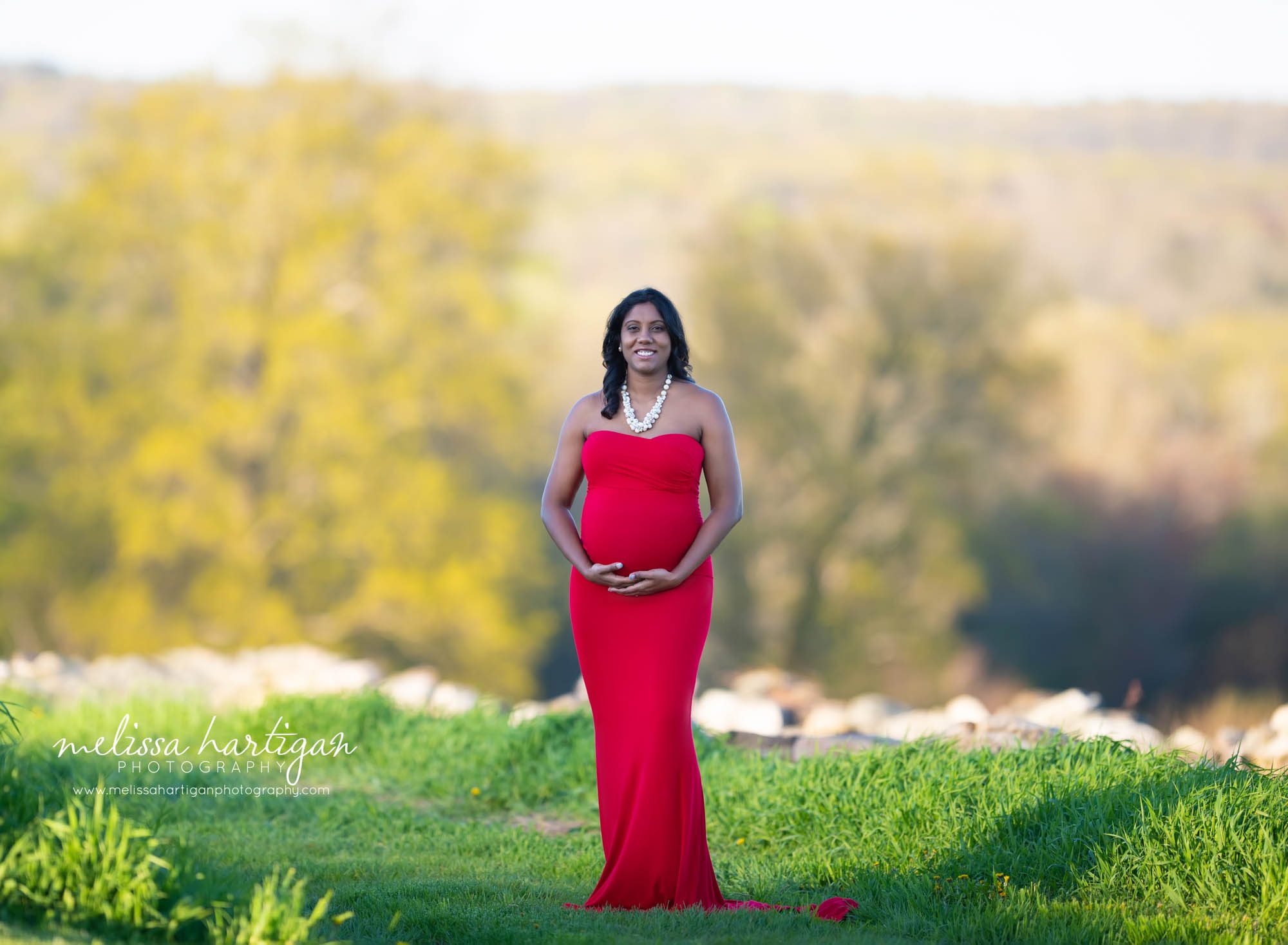 Pregnant mom standing maternity photography pose wearing long fitting red dress