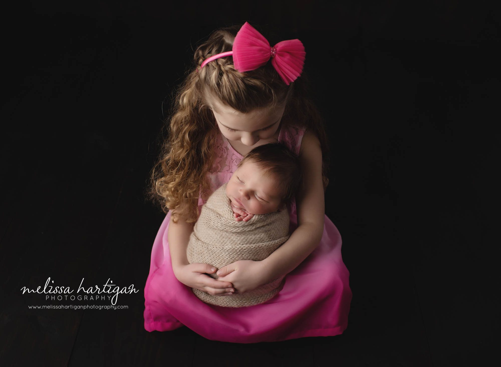older sister holding baby brother in newborn photoshoot studio pose