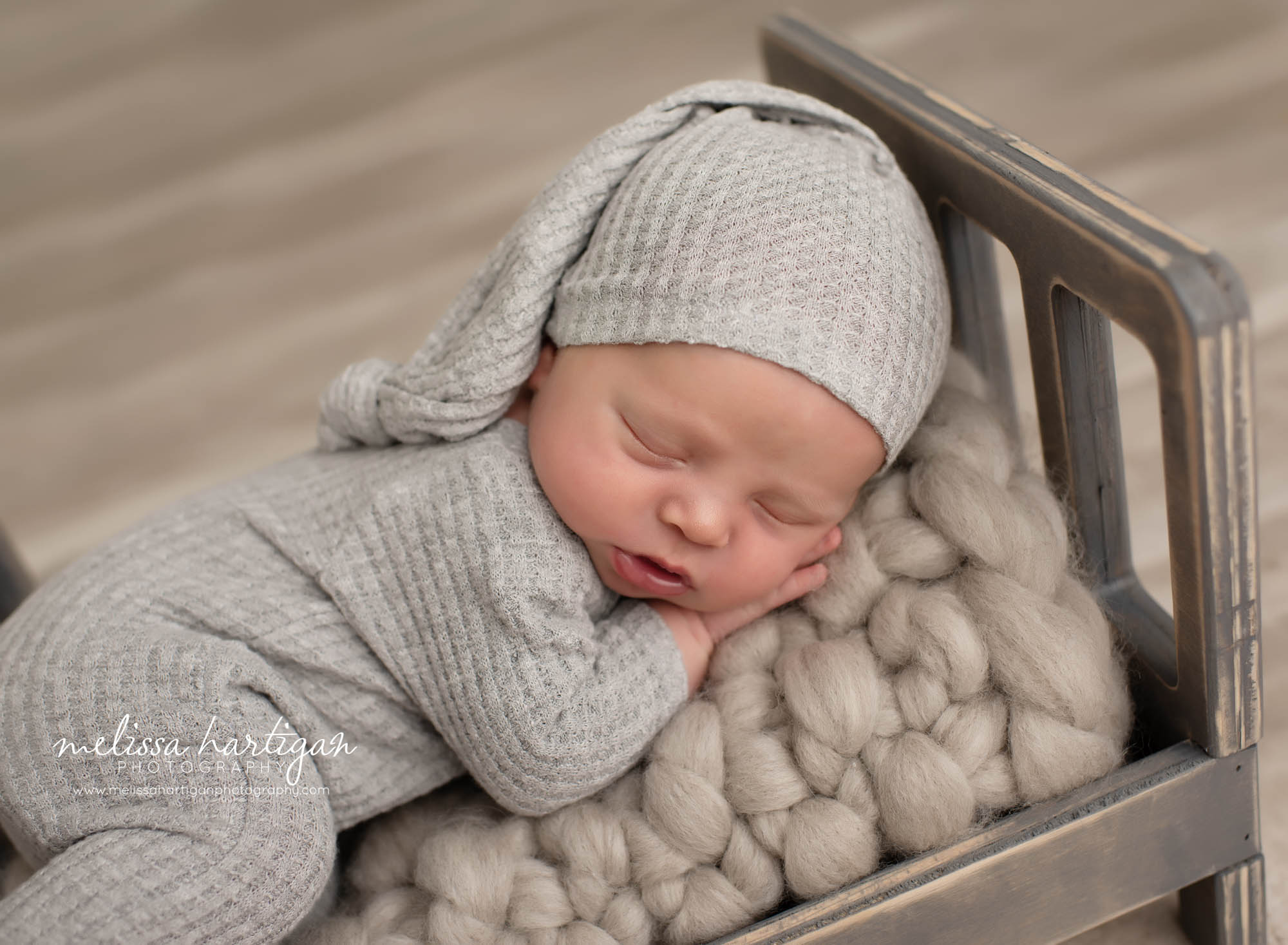 Baby boy posed in wooden bed wearing gray newborn outfit and sleepycap Newborn photographer CT