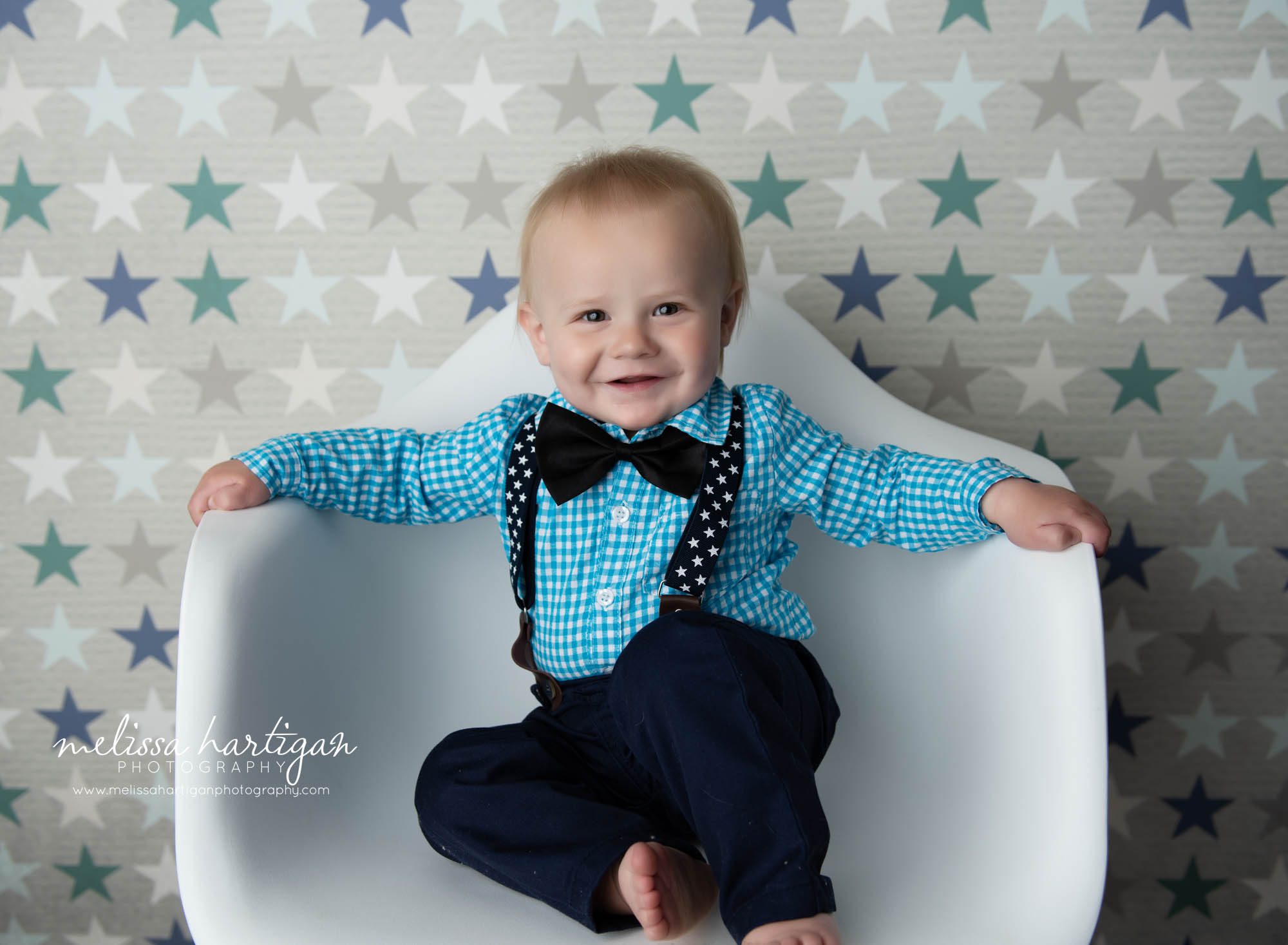 baby boy sitting on white chair wearing blue shirt with star suspenders