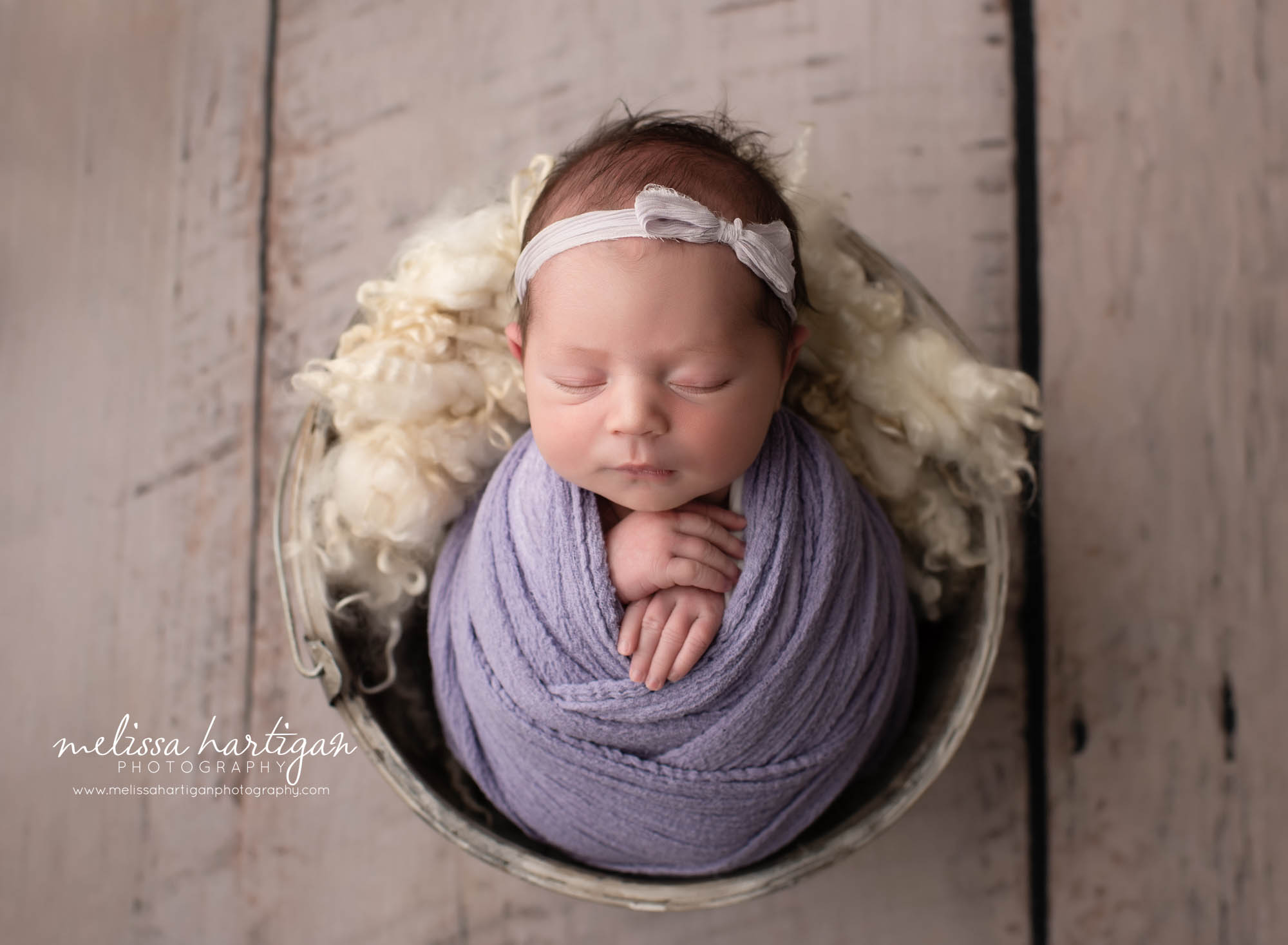 Baby girl wrapped in purple wrap with purple headband posed in bucket Connecticut newborn photographer