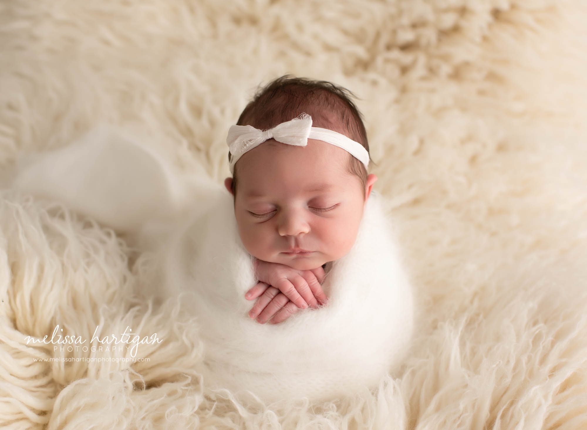 baby girl wrapped in white wrap on cream flokati
