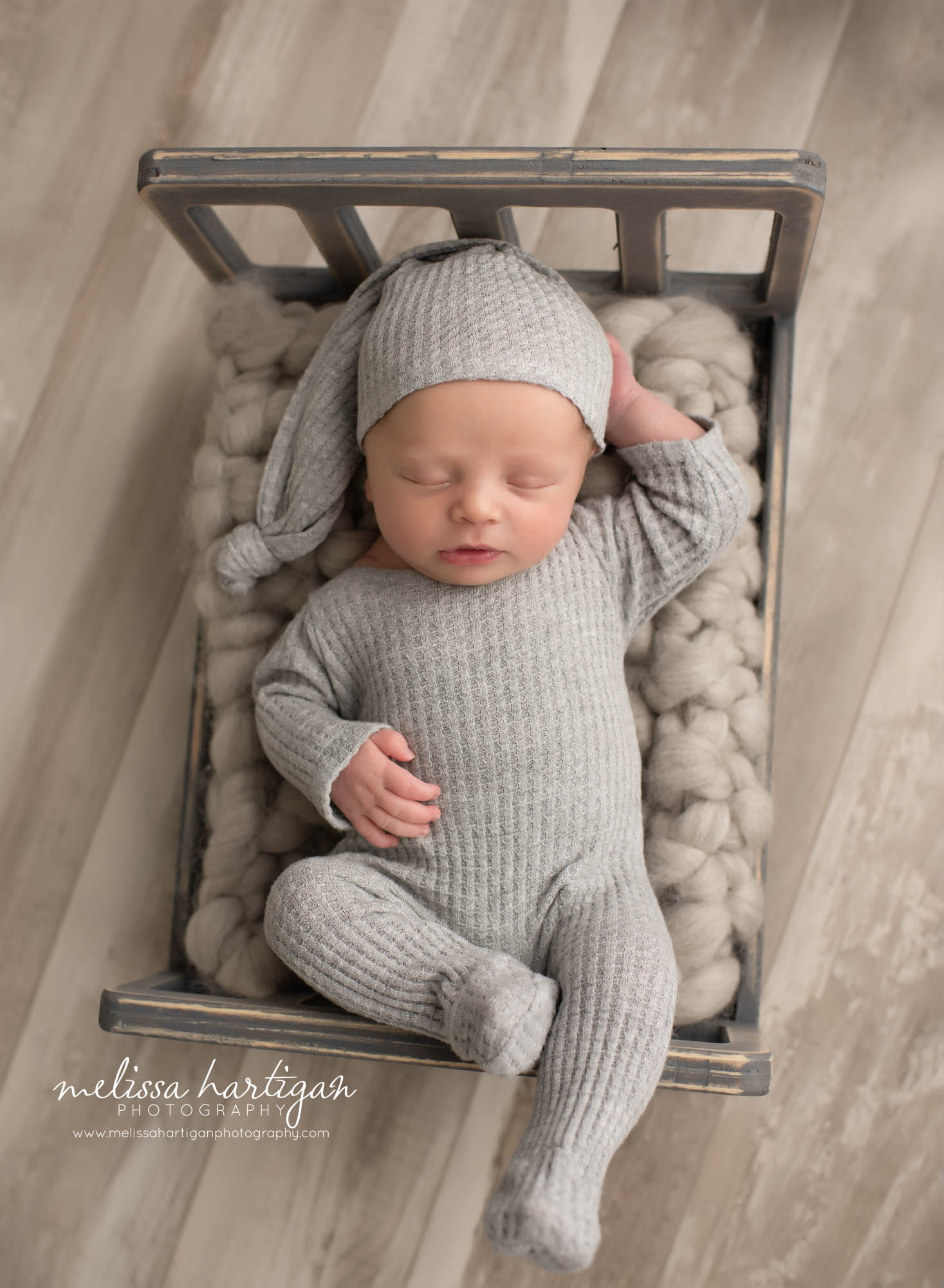 baby boy posed on back wearing gray footed outfit and sleepy cap