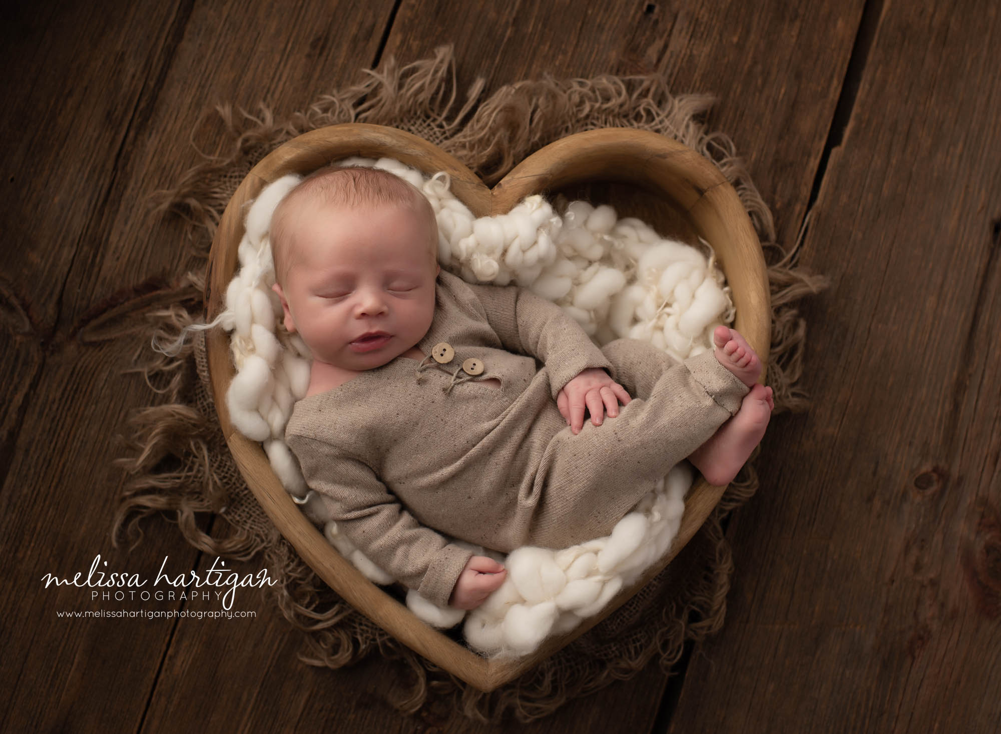 newborn baby boy posed in wooden heart prop with tan outfit on