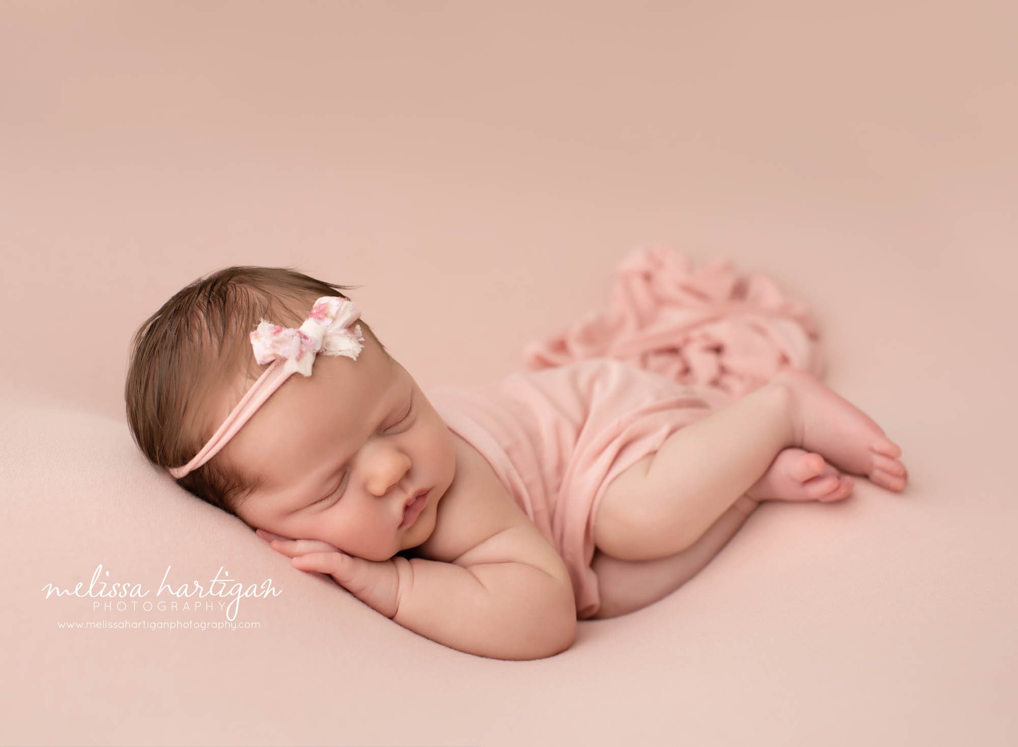 baby girl posed on pink backdrop with pink wrap and bow headband CT newborn photography