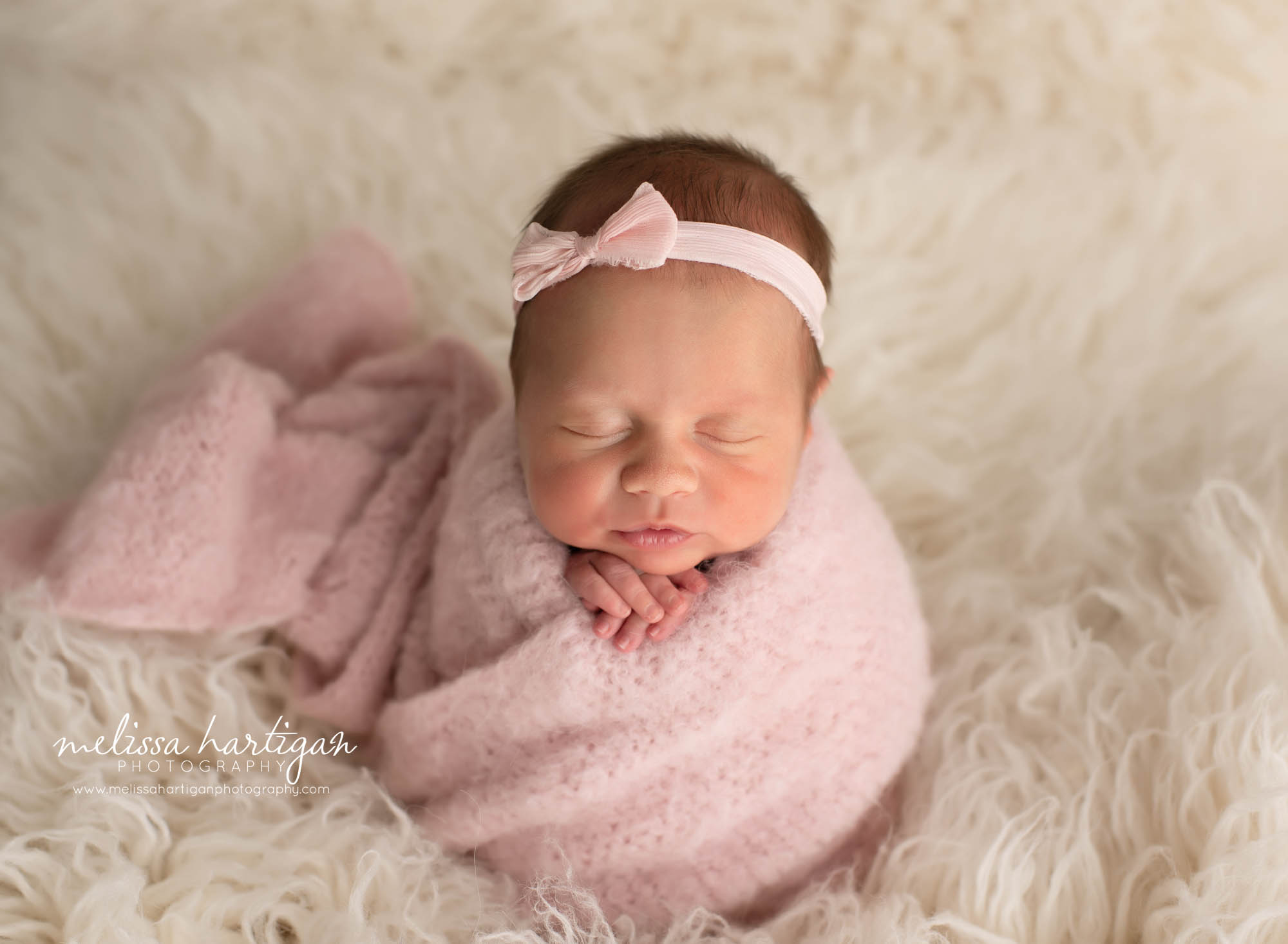 baby girl wrappe din light pink knitted wrap with pink bow headband on cream flokati