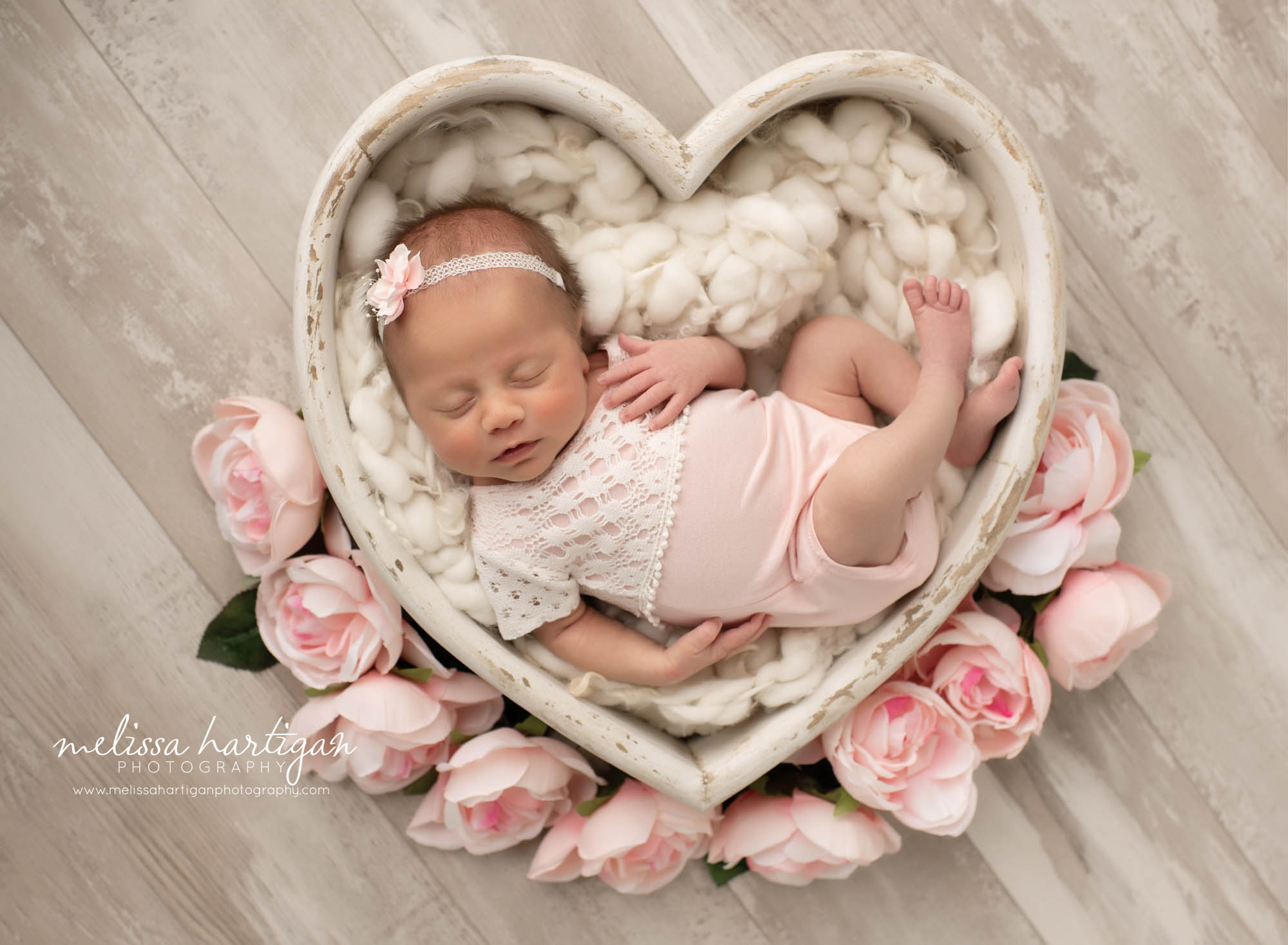 Baby girl posed in white wooden heart shaped prop with rose flora around the sides CT newborn Photograpy