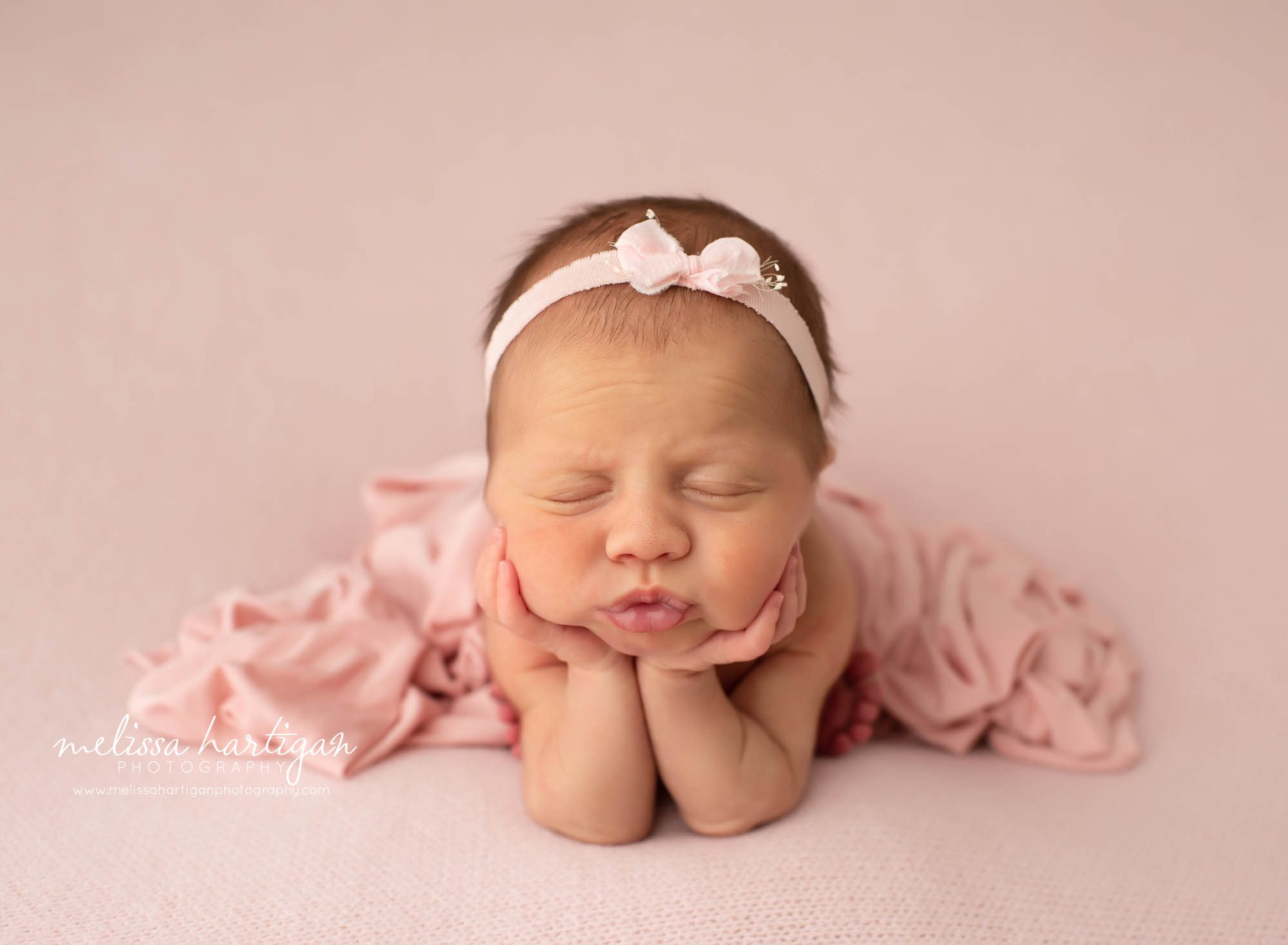 newborn baby girl posed froggy posed on pink backdrop with light pink bow headband