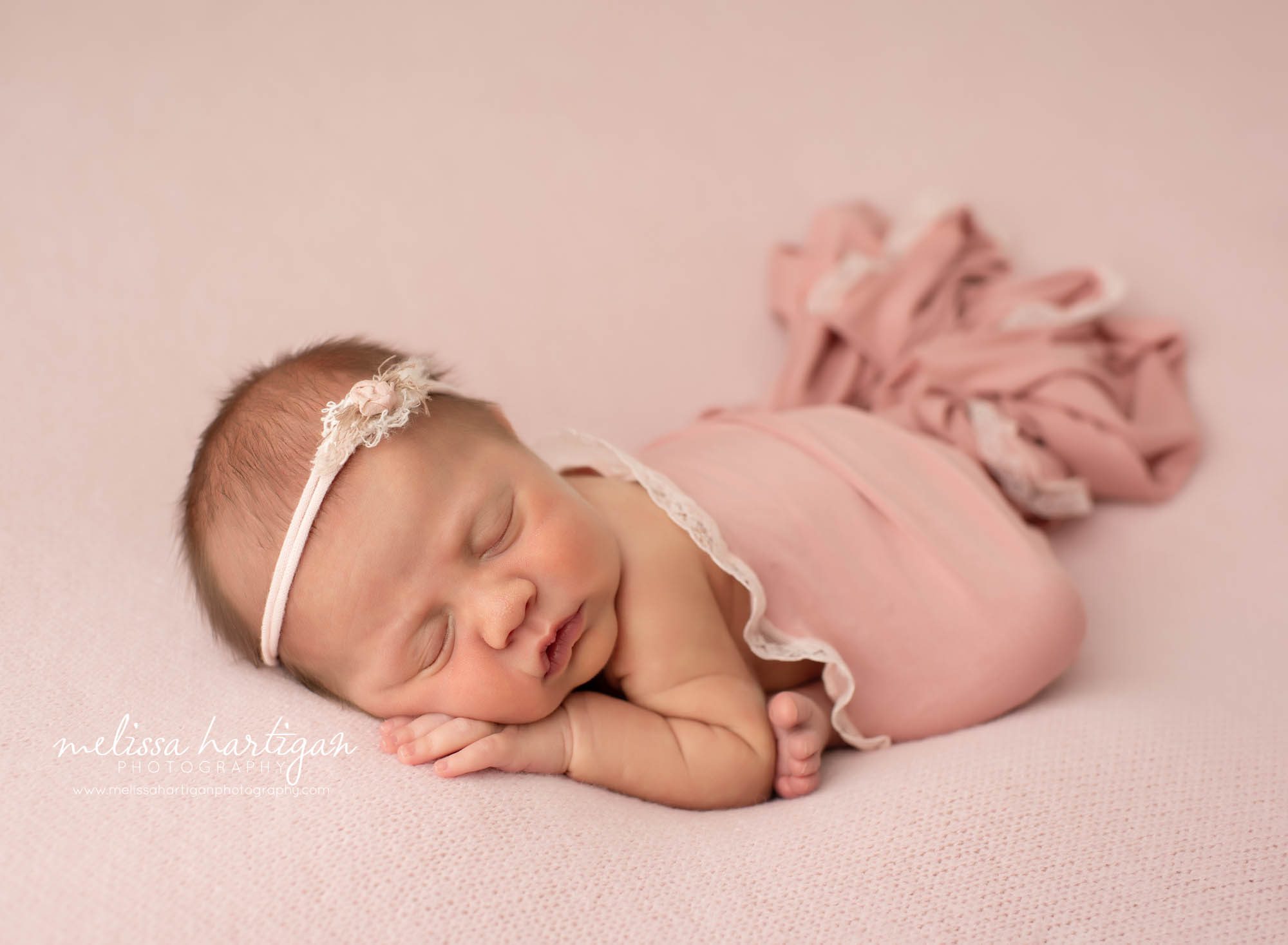 newborn girl posed modified taco posed on light pink backdrop with pink lace wrap