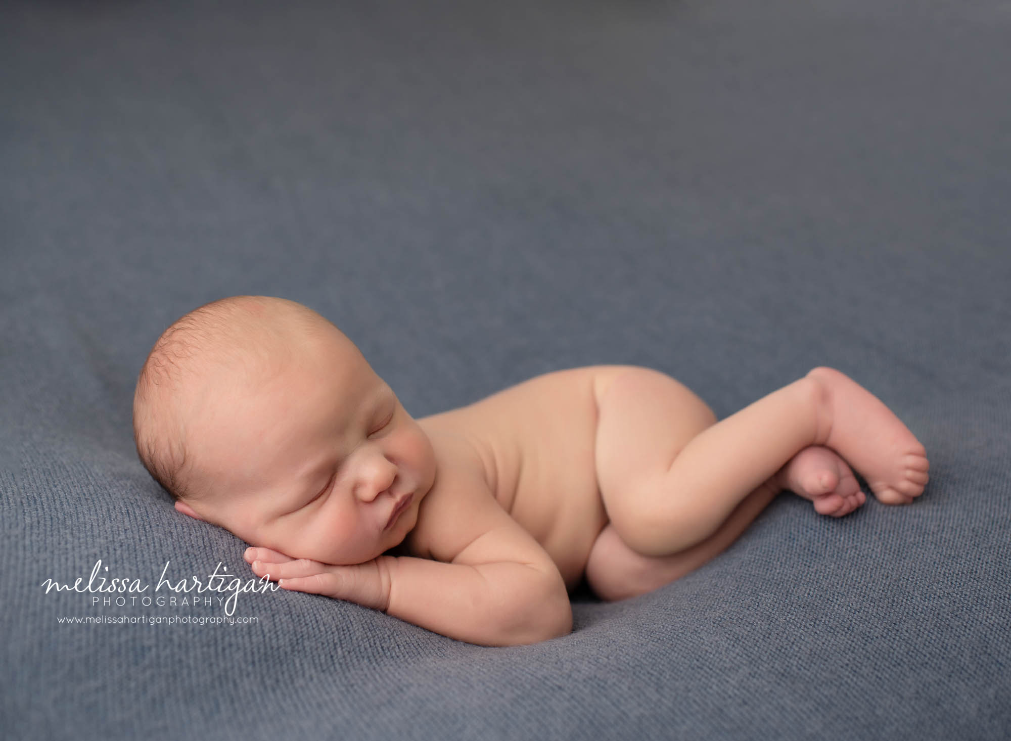 newborn baby boy posed on side on denim blue backdrop