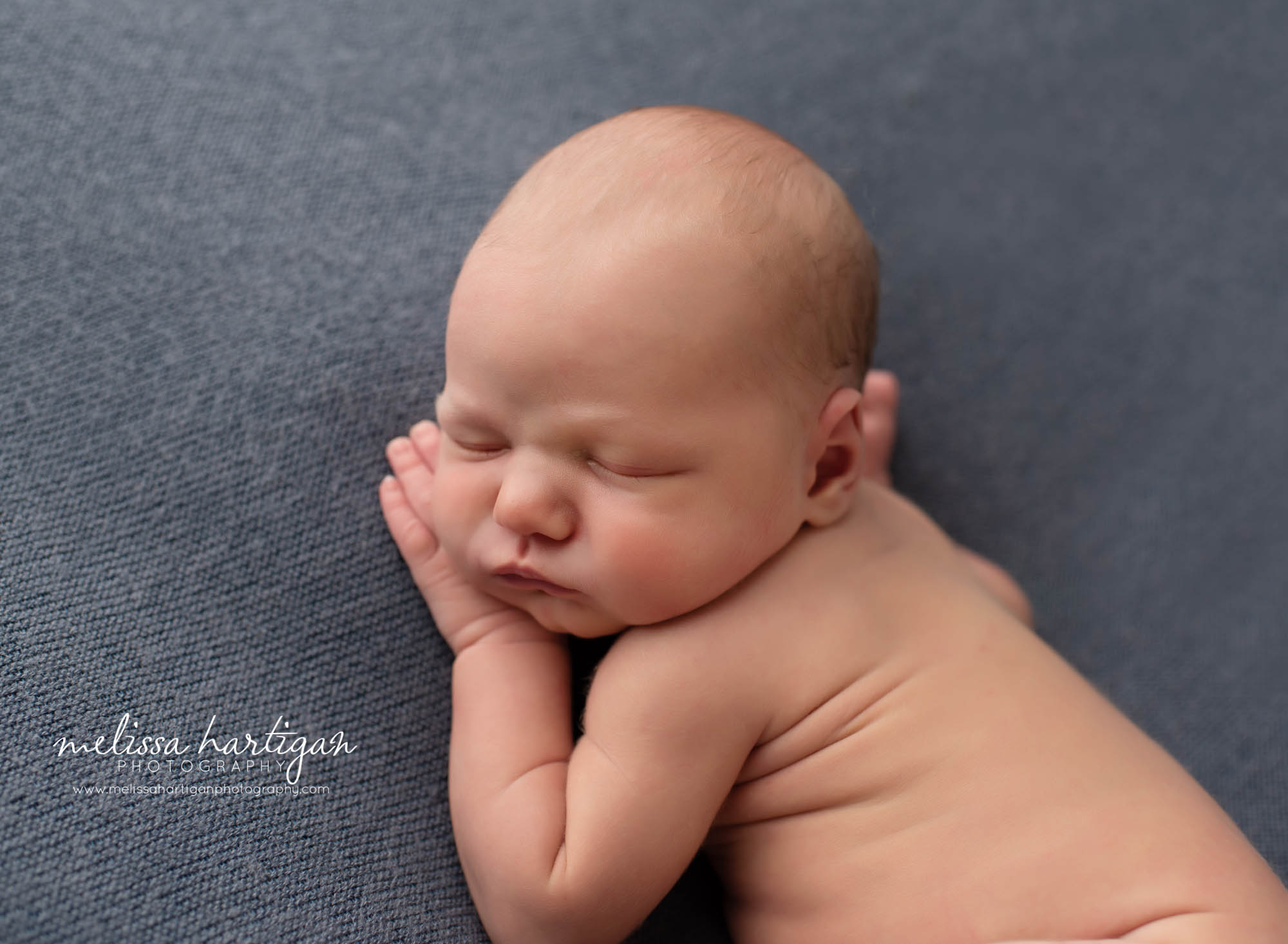 baby boy posed with hand under cheek on denim blue posing backdrop tolland Ct newborn photography