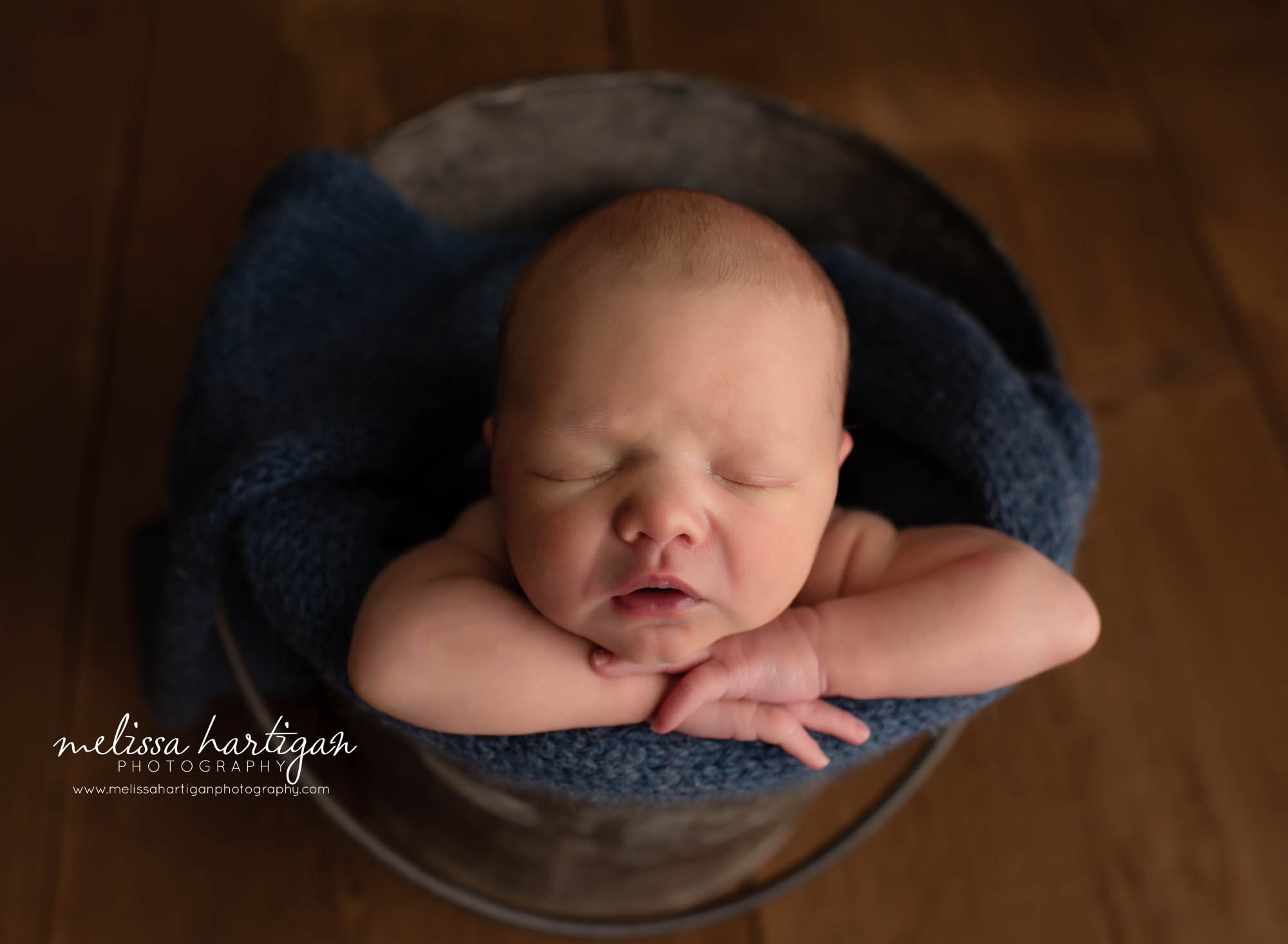 posed newborn photography baby posed in metal bucket with navy blue knitted wrap