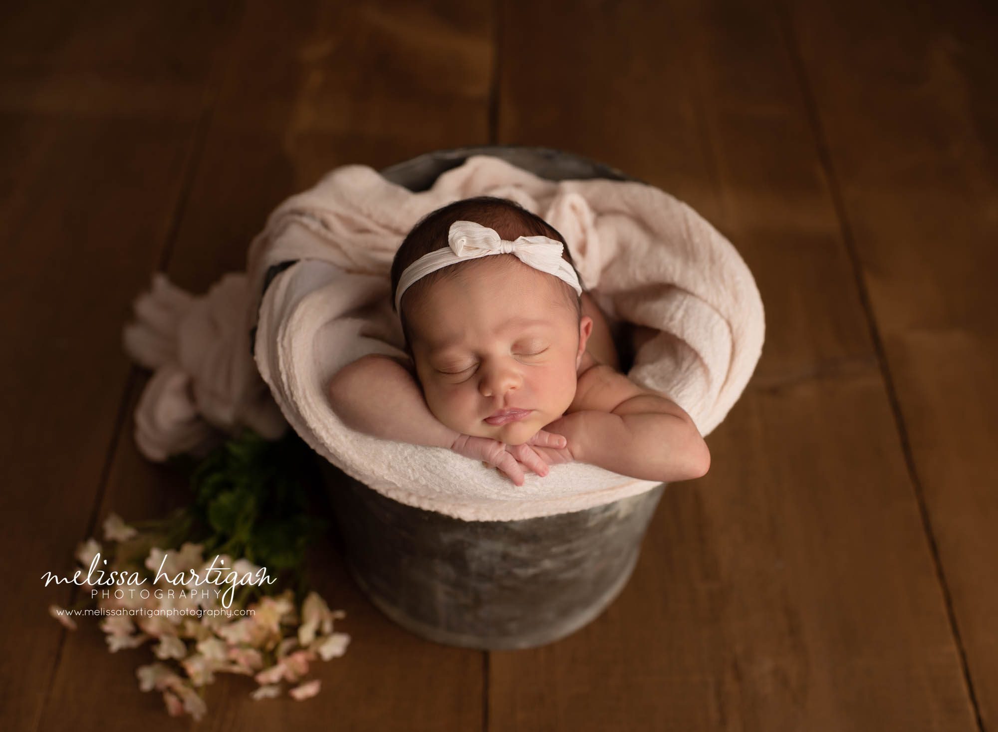 newborn baby girl posed in bucket with blush pink wrap and peach flowers on wooden boards