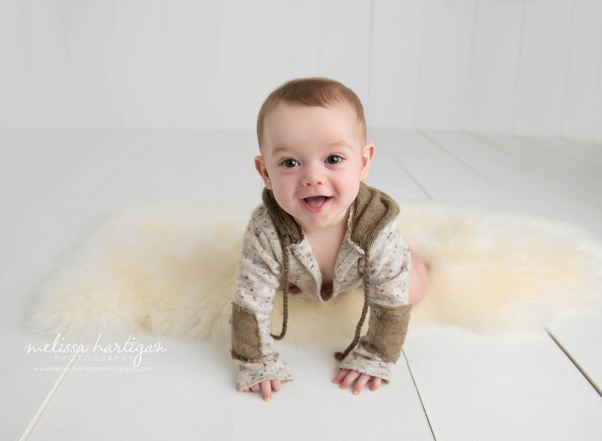 baby boy crawling on white furry rug and white wooden boards in photography studio