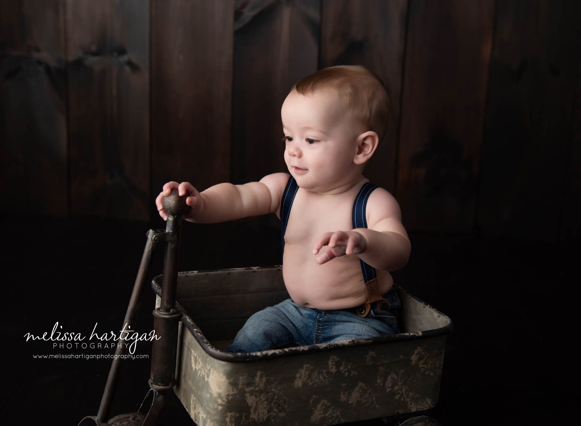 baby boy sitting in metal pulley cart with suspenders on