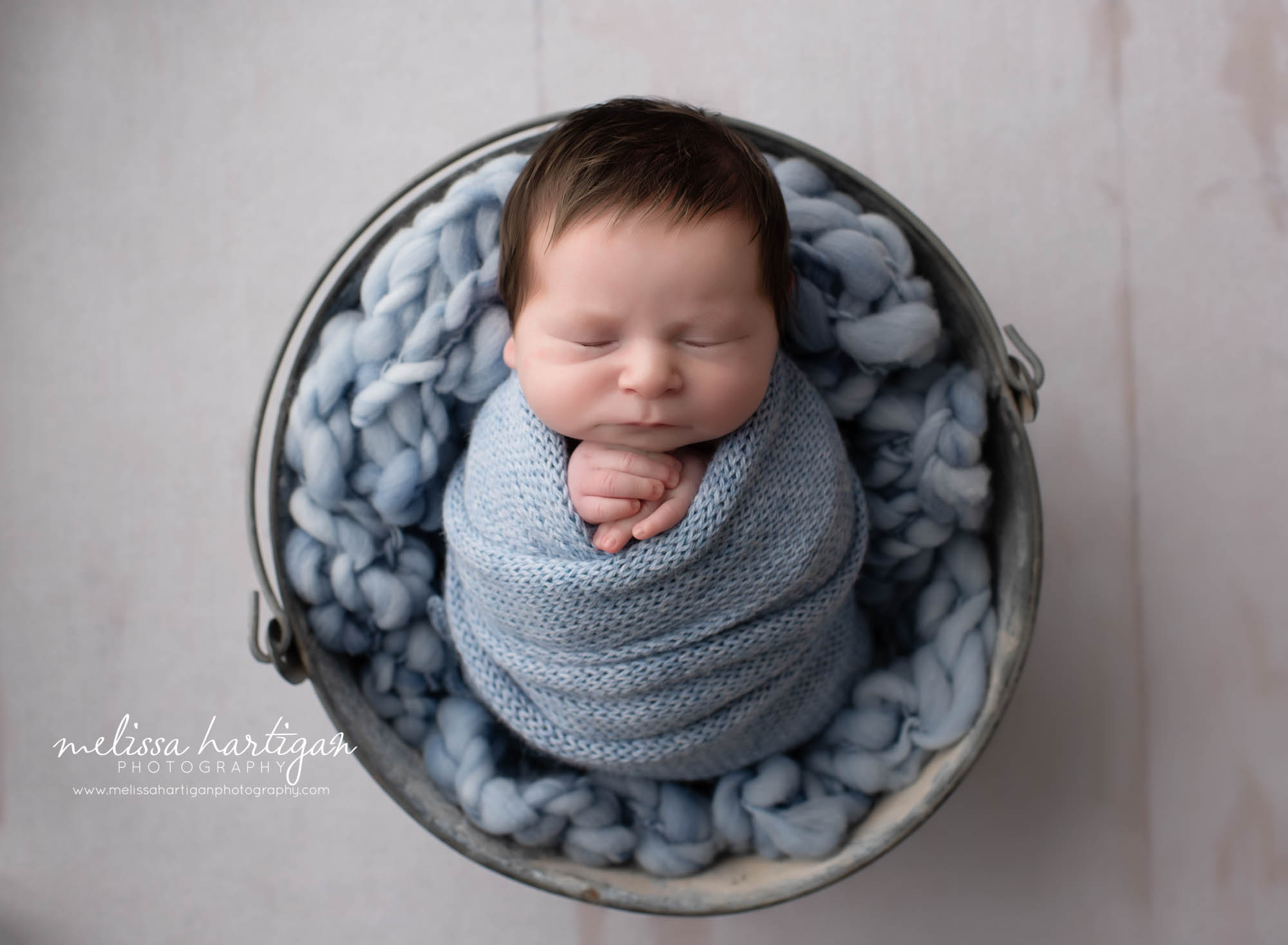 Newborn baby boy wrpaped in knitted blue wrap with blue chunky layer in metal bucket