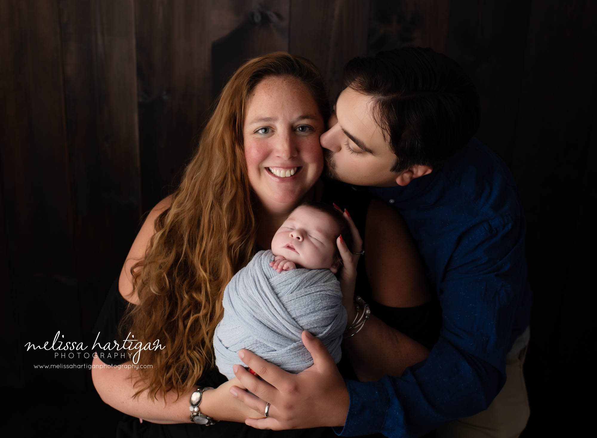 dad kissing mom both holding newborn son