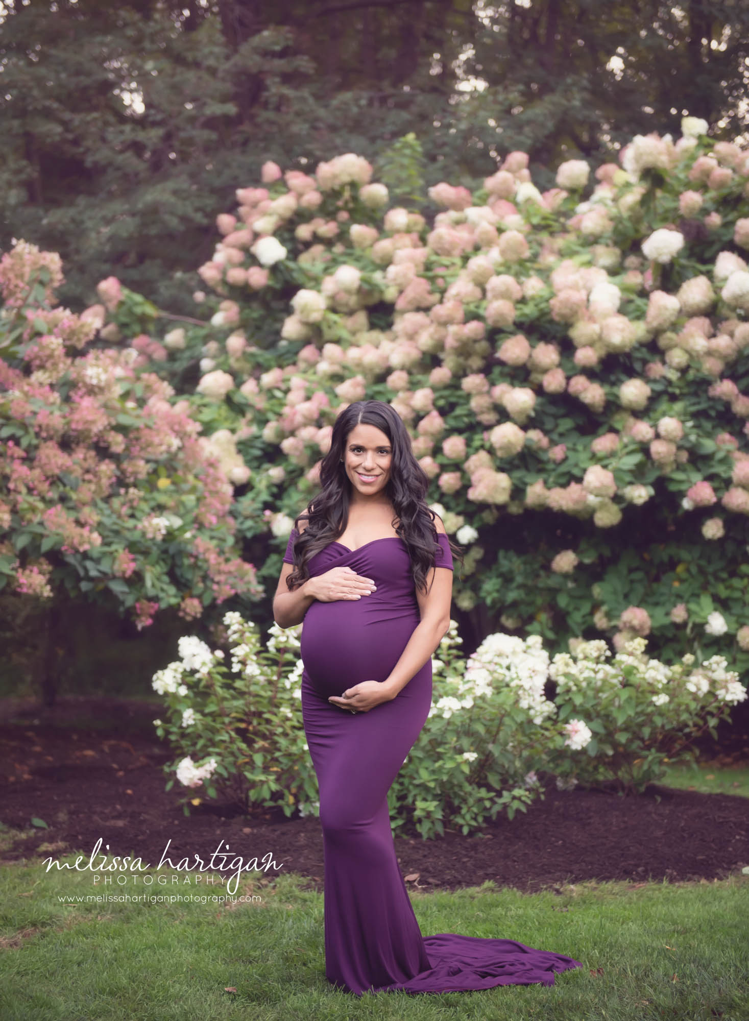 pregnant mom standing holding belly looking at camera with flowers in the background East Hartford CT Maternity Photographer