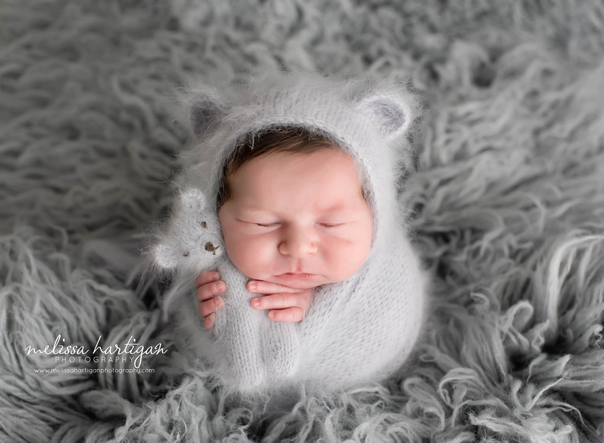 baby boy wrapped in light grey wrap with matching bear bonnet and knitted teddy bear