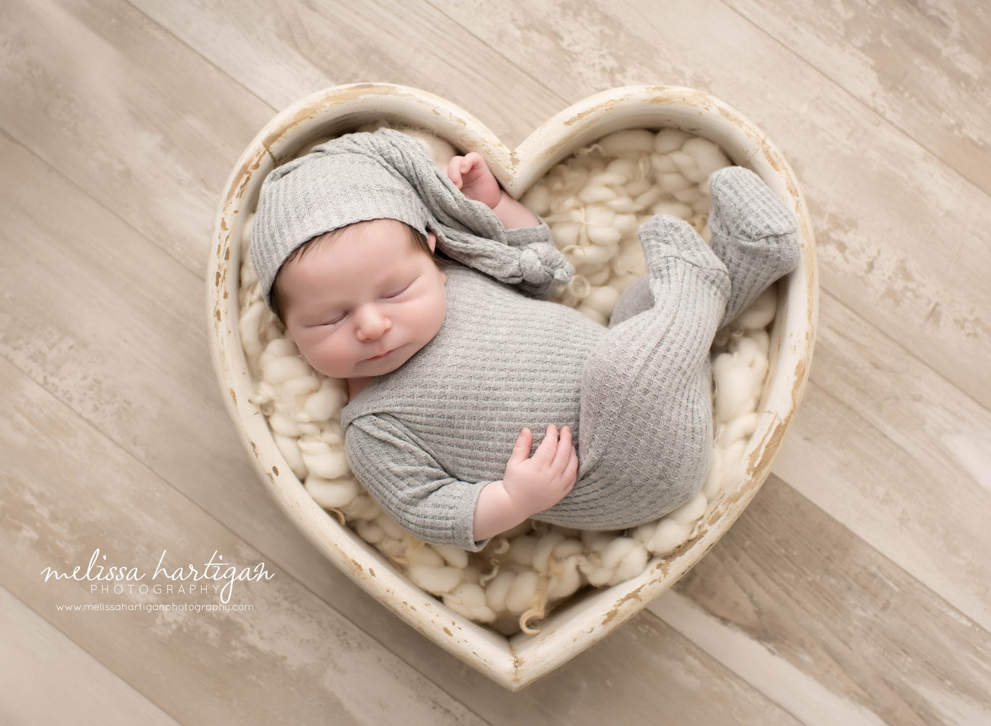 baby boy wearing grey footed sleeper with sleepy cap posed in wooden heart prop Ellington CT newborn photography