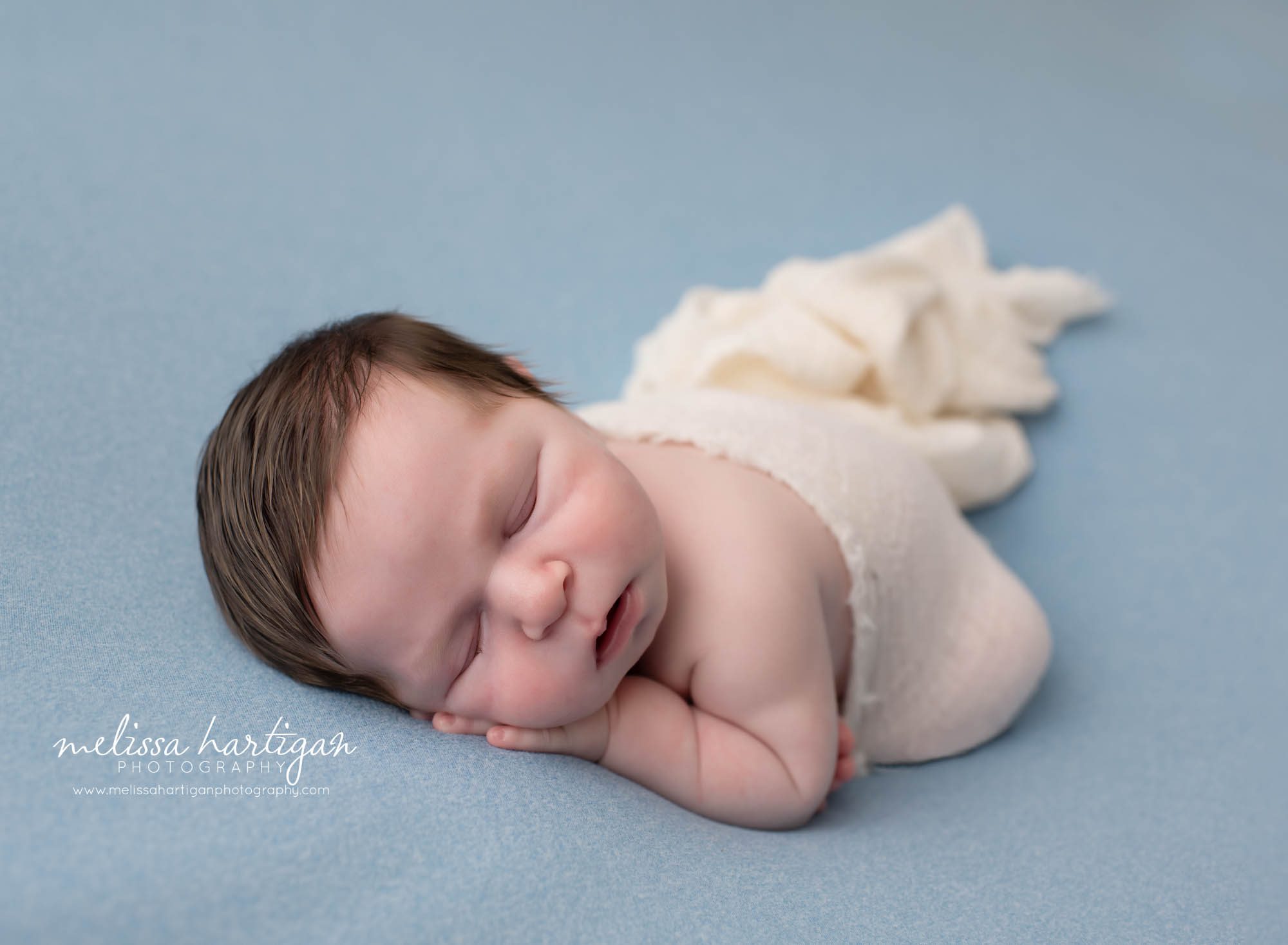 baby boy posed on blue backdrop with cream layer wrap