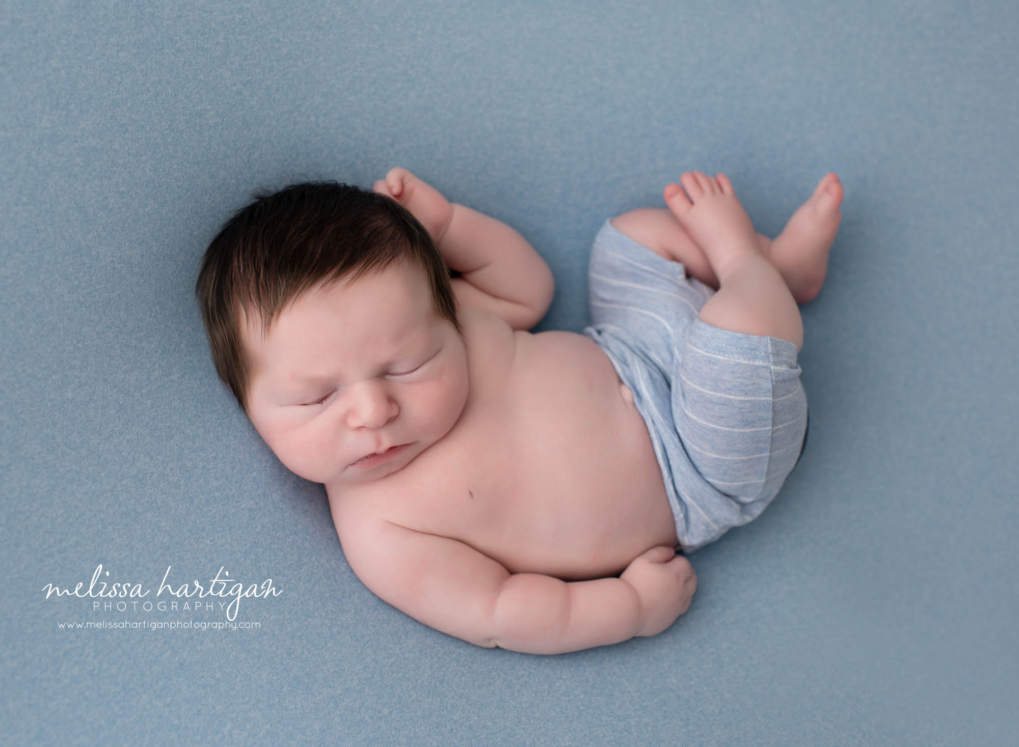 baby boy posed curled up on blue posing backdrop
