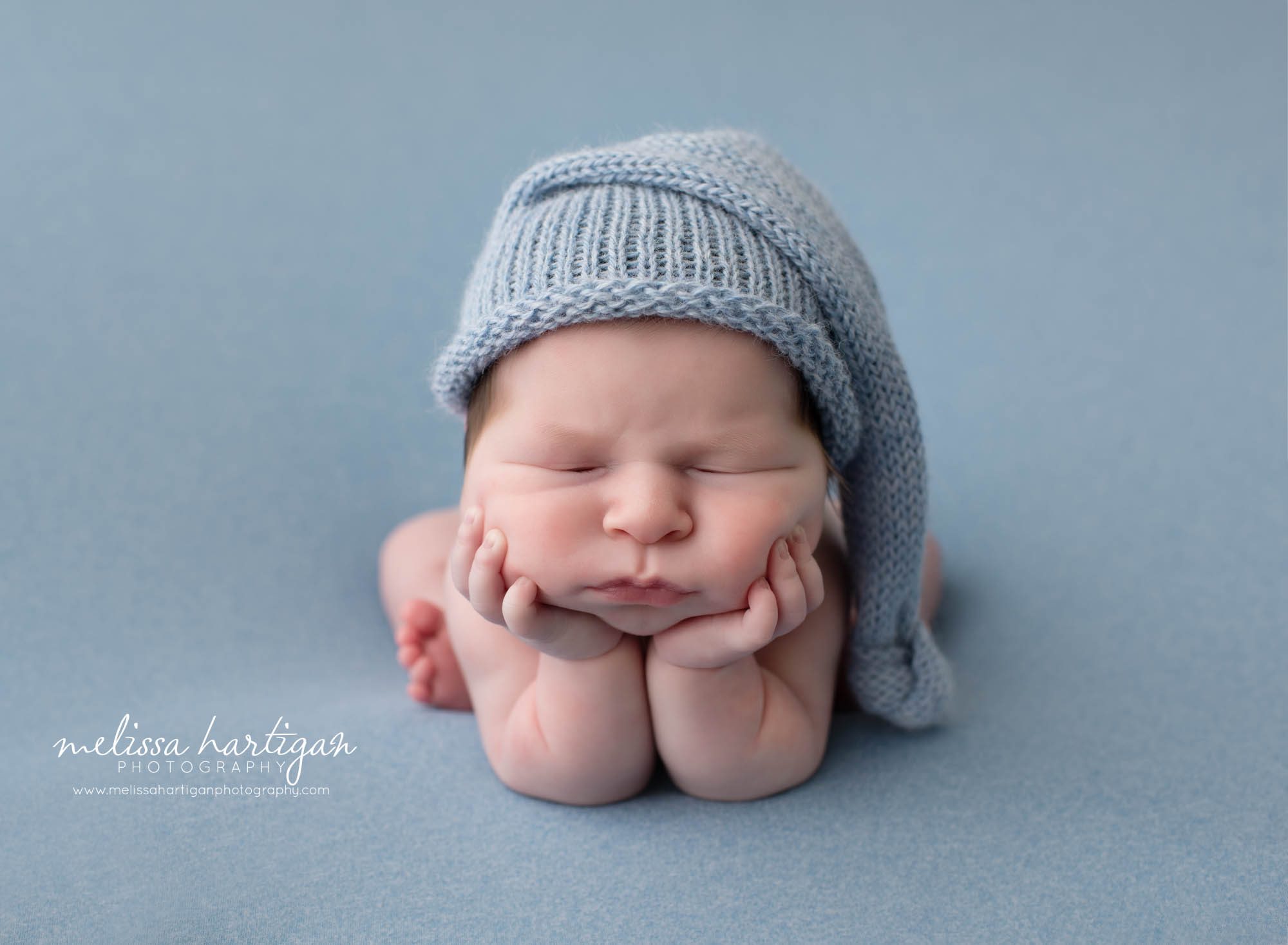 baby boy froggy pose on blue backdrop with knitted blue sleepy cap