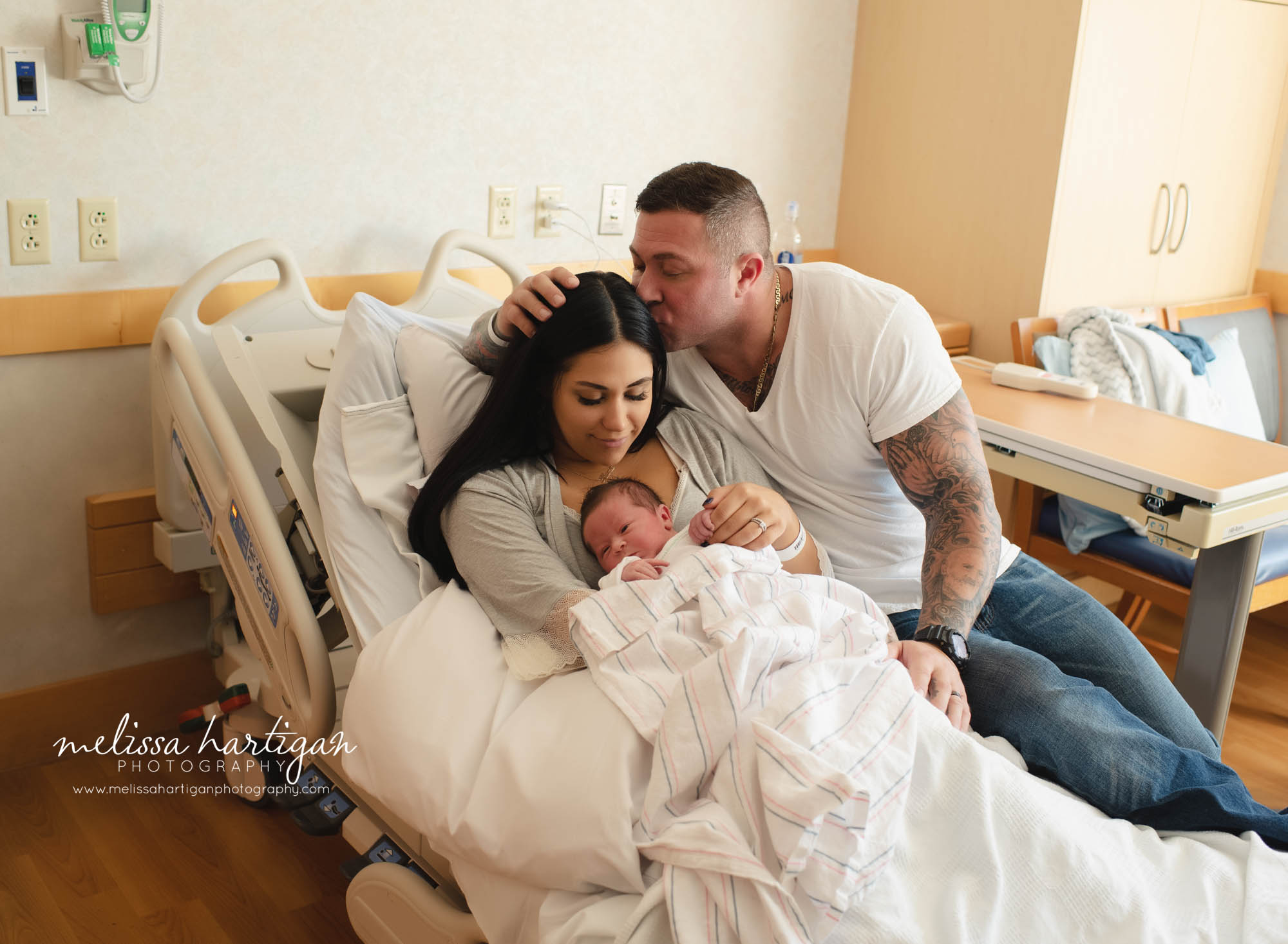 dad giving mom a kiss on side of head while holding newborn baby boy