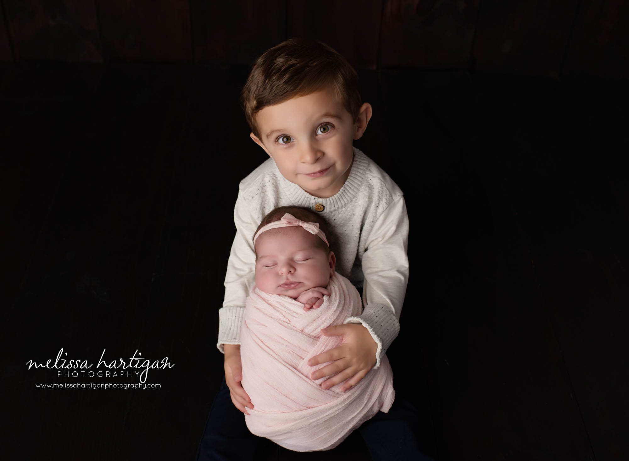 big brother holding newborn baby sister wrapped in pink wrap