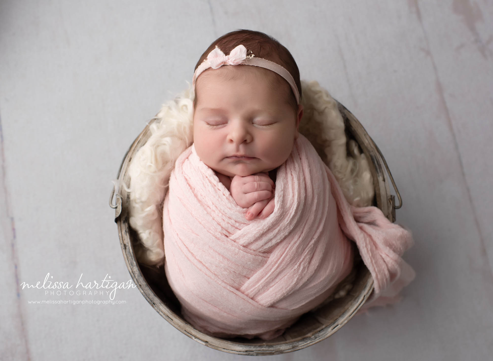 newborn baby girl wrapped in light pink wrap posed in buket with light pink fluff