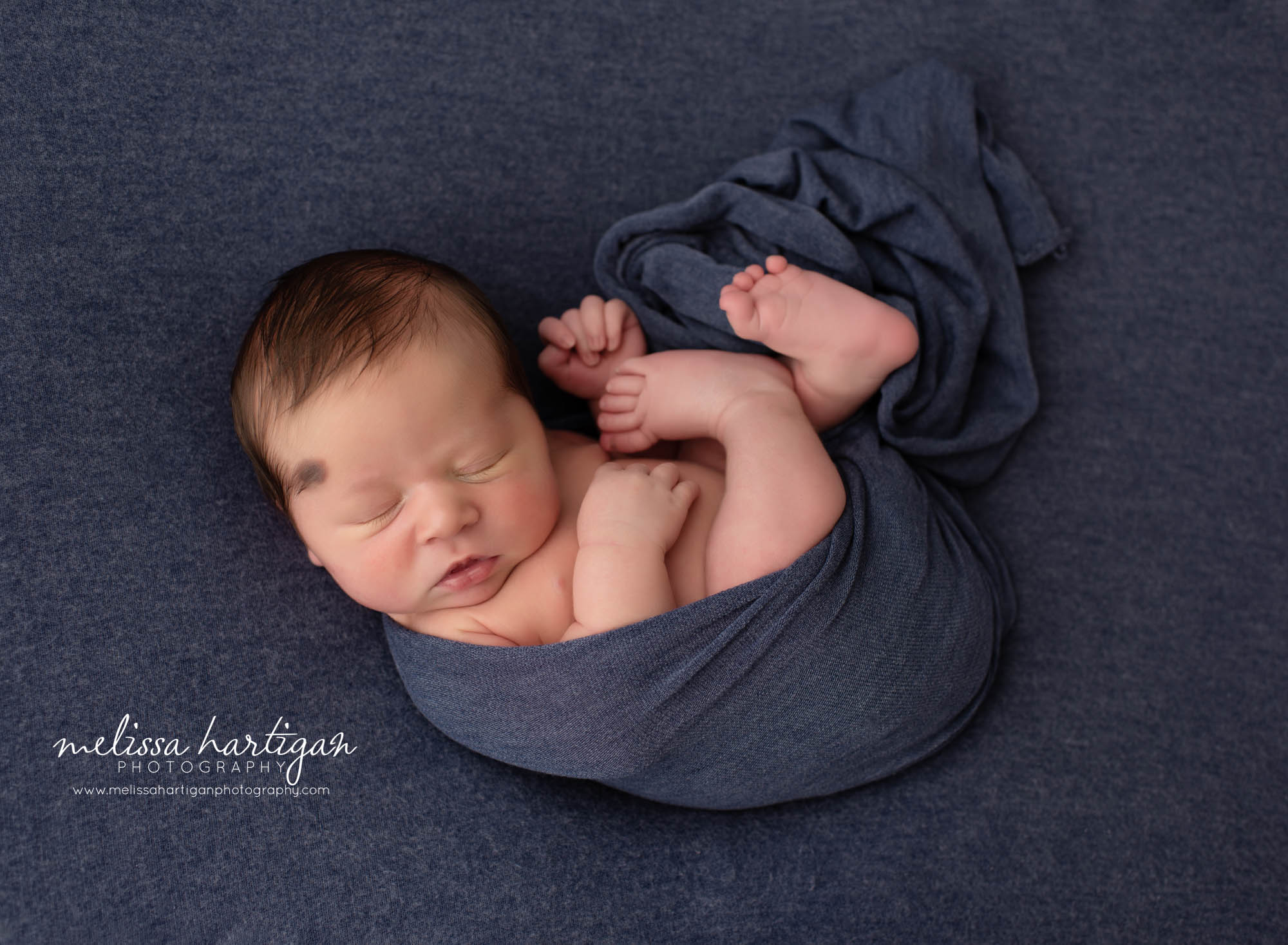 newborn baby boy wrapped in navy blue wrap on back posed newborn photography