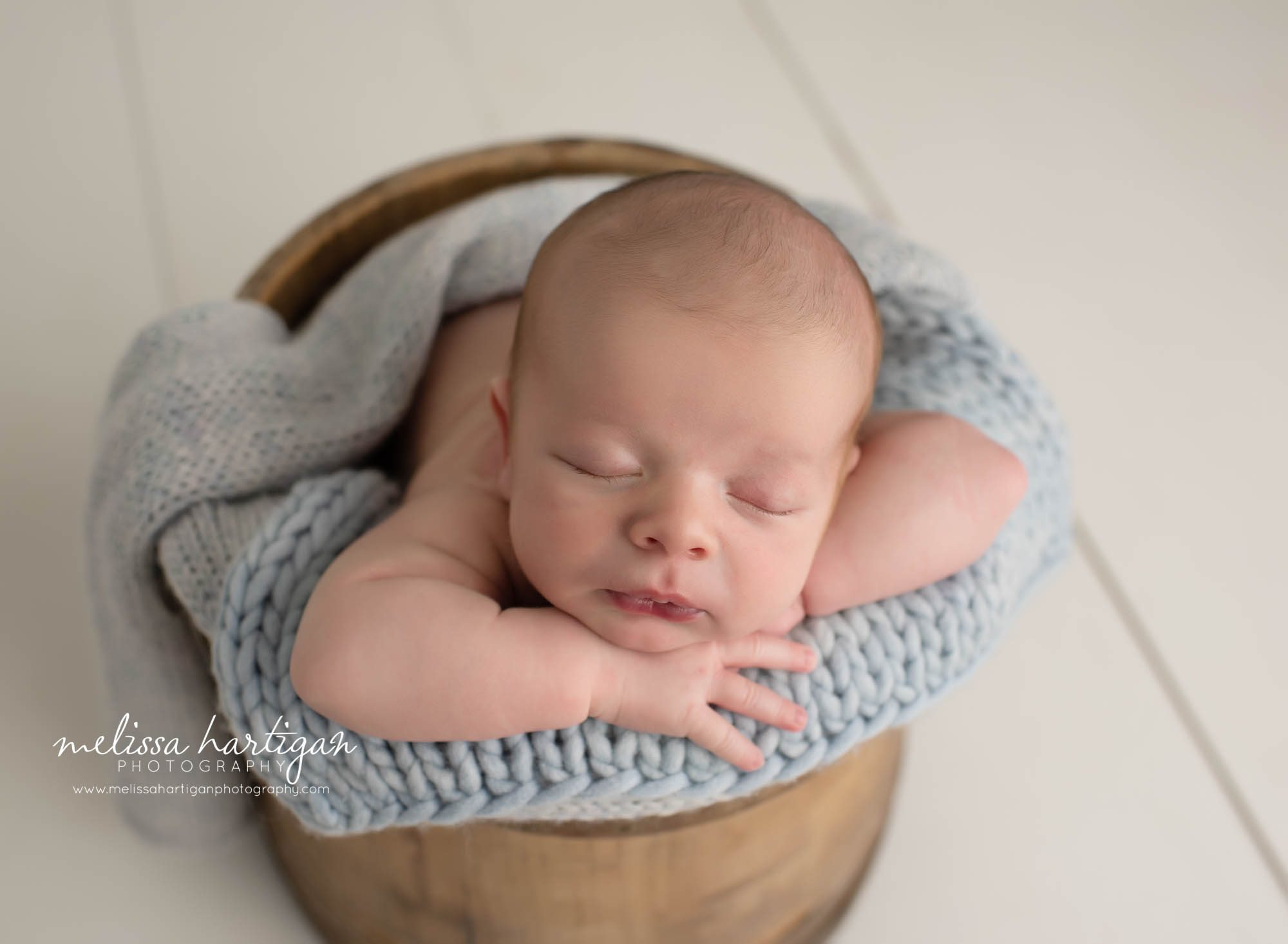 Newborn boy posed in wooden bucket with blue knitted layer