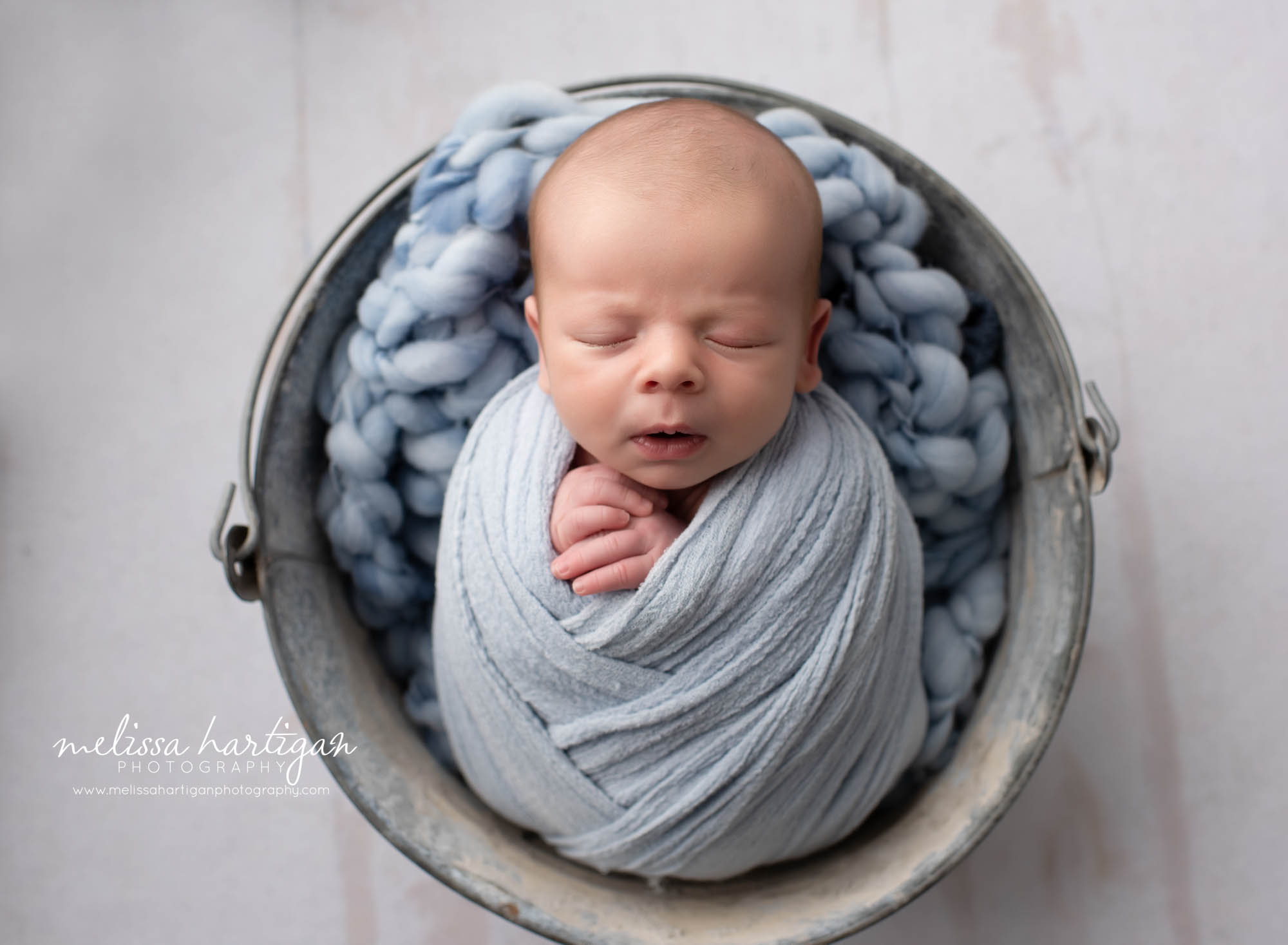 Newborn boy wrapped in metal bucket with blue knitted layer