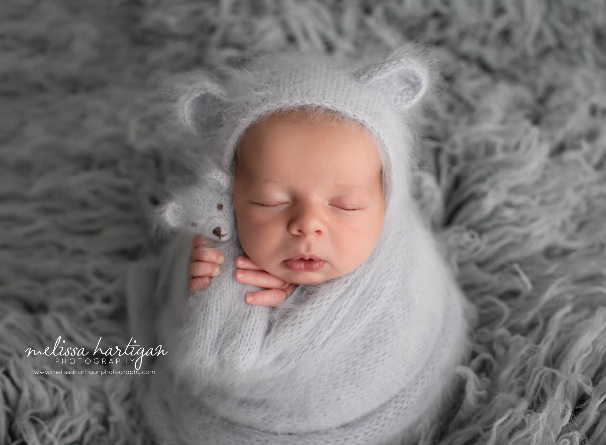 newborn boy posed on flokati with knitted wrap and matching bear bonnet and knitted teddy bear