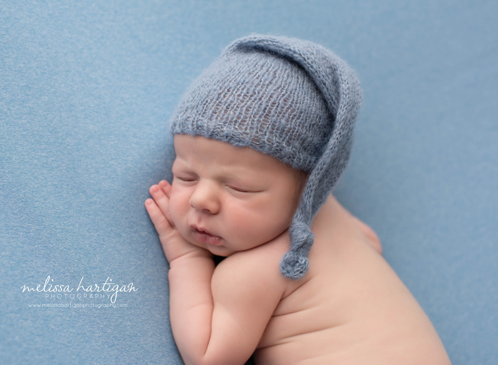 Newborn boy posed on blue backdrop with blue knitted sleepy cap