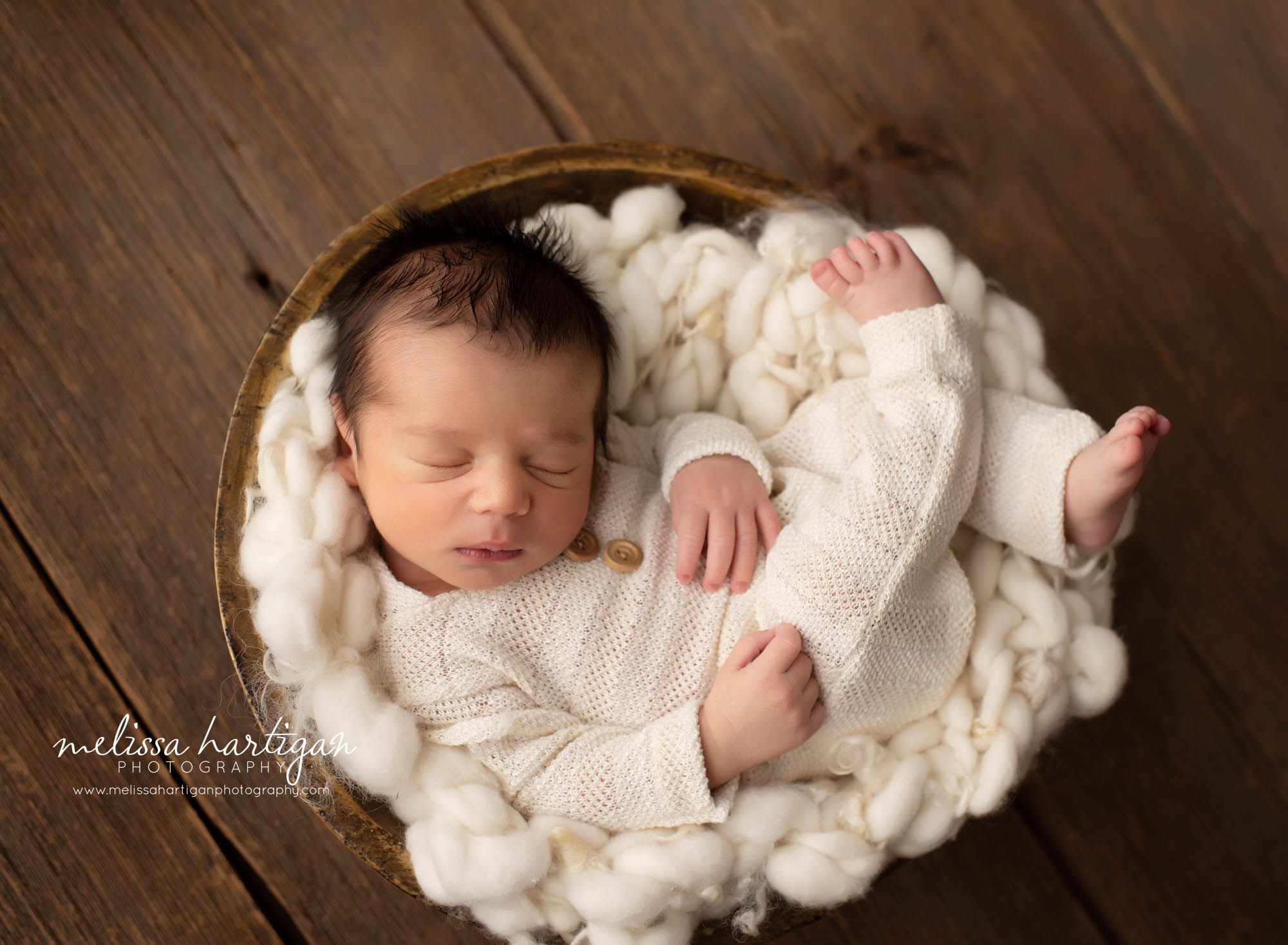 Newborn baby boy wearing newborn outfit posed curly in wooden bowl