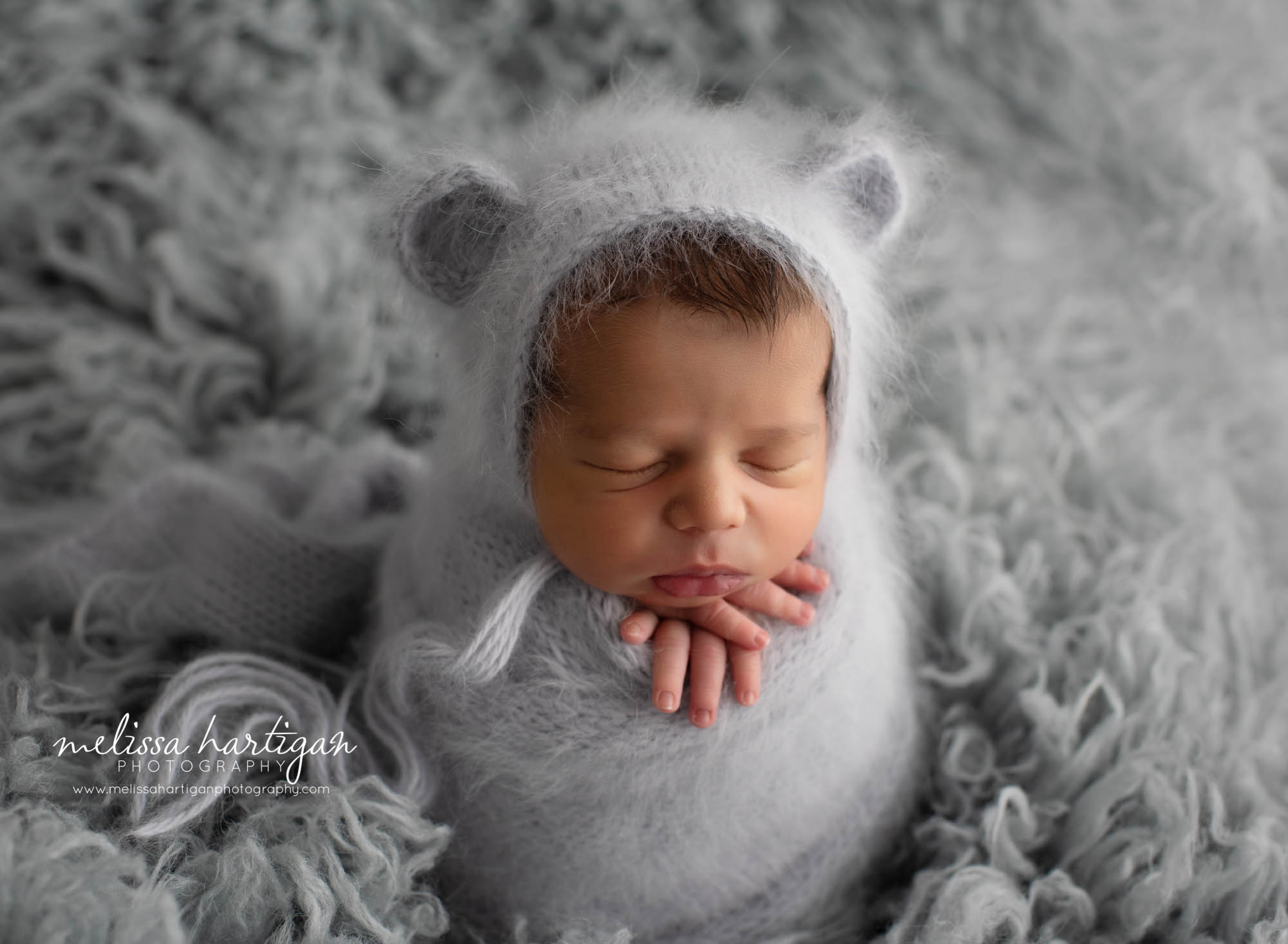Newborn baby boy wrapped in grey knitted wrap with matching knitted bear bonnet