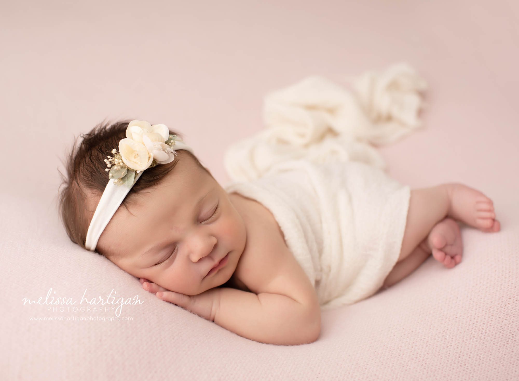 newborn baby girl pose don light pink backdrop with cream wrap draped over and cream floral headband