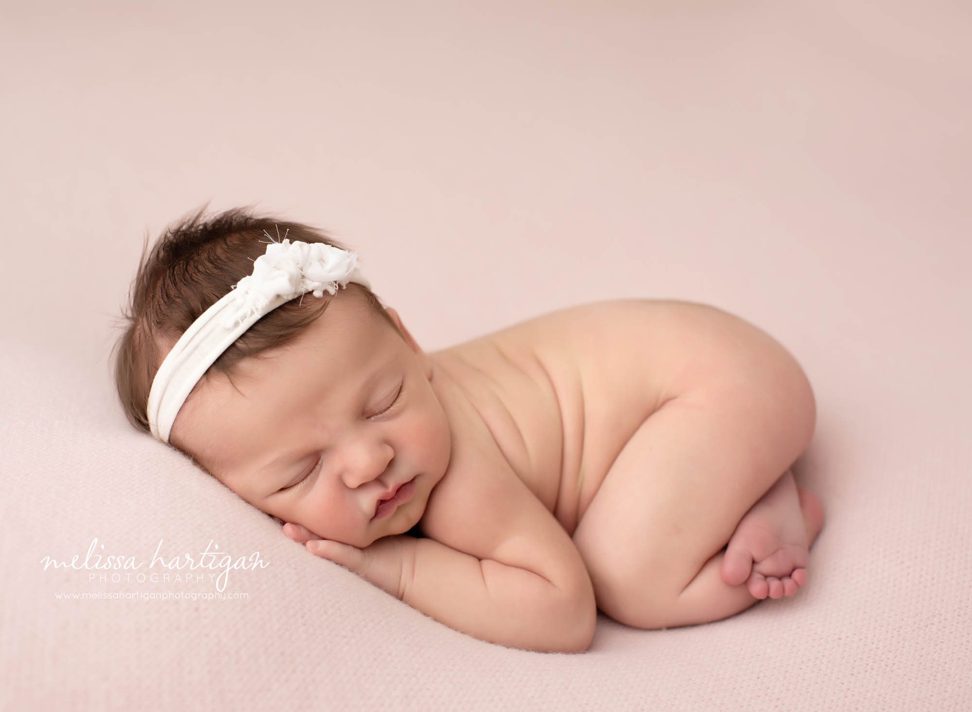 baby girl posed on tummy with cream flower headband and soft pink backdrop