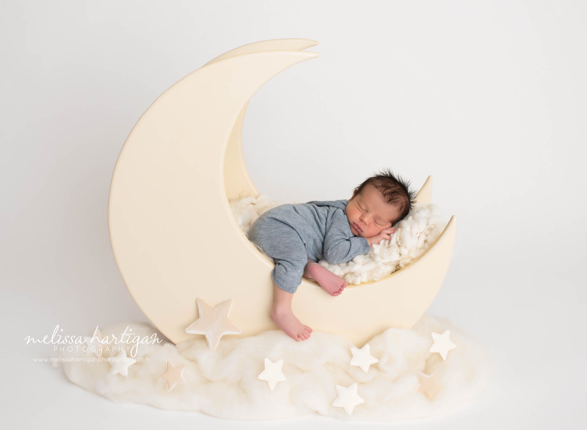 newborn boy posed on wooden moon prop wearing blue newborn outfit