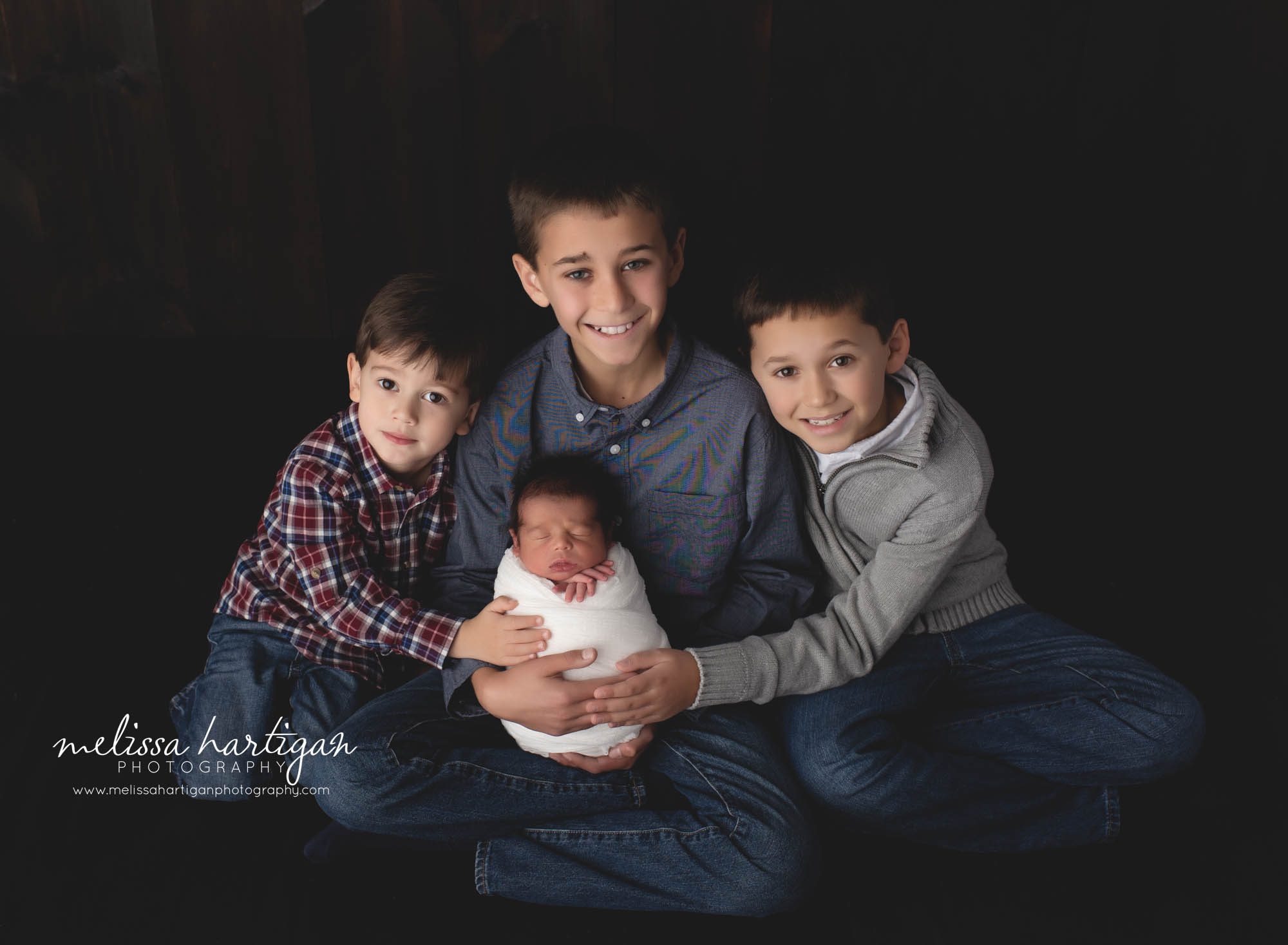 three older siblings holding their baby brother in studio family photography pose newborn session