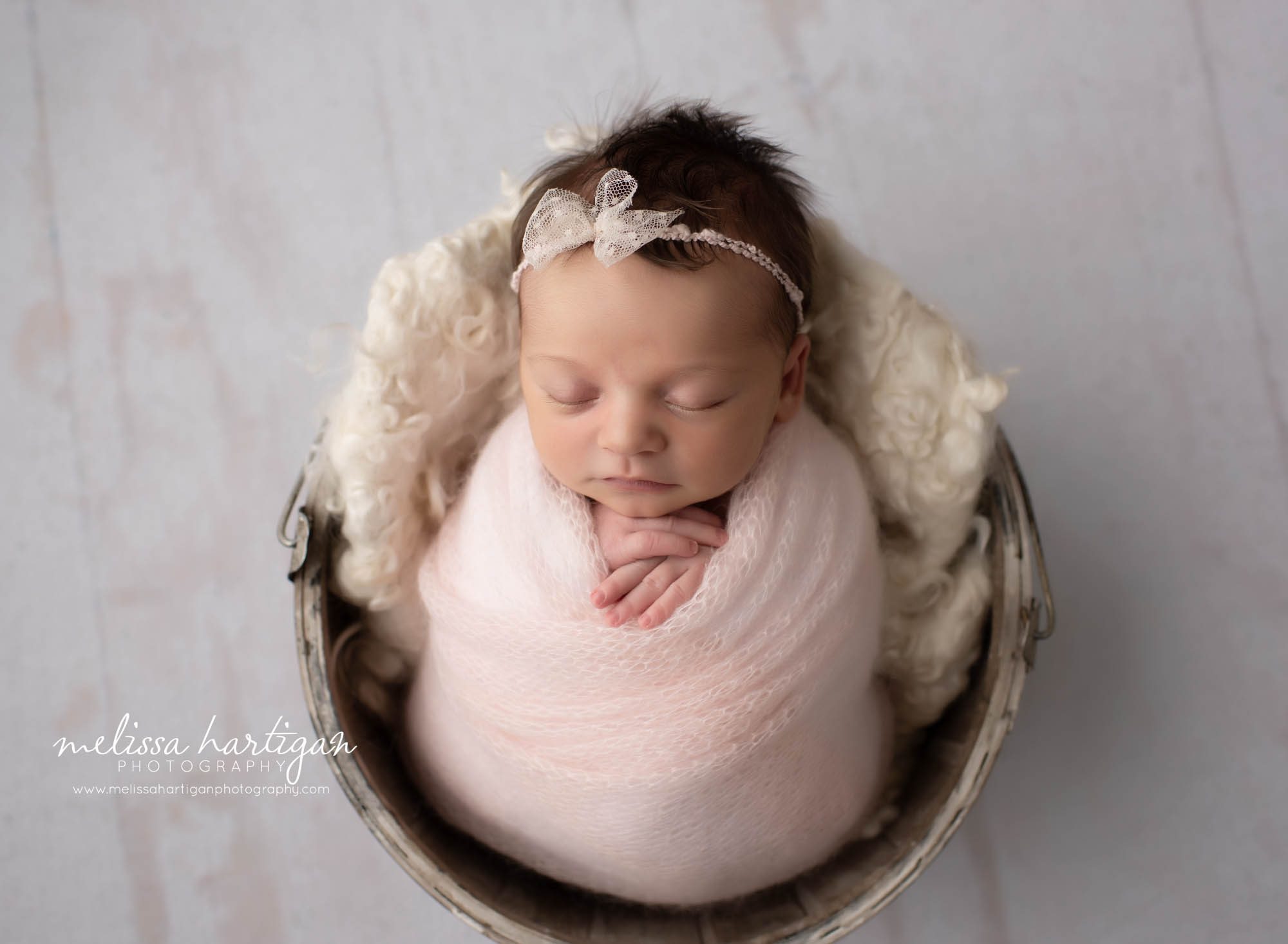 baby girl wrapped in soft and and light pink wrap posed in bucket with cream curly layer newborn photography CT