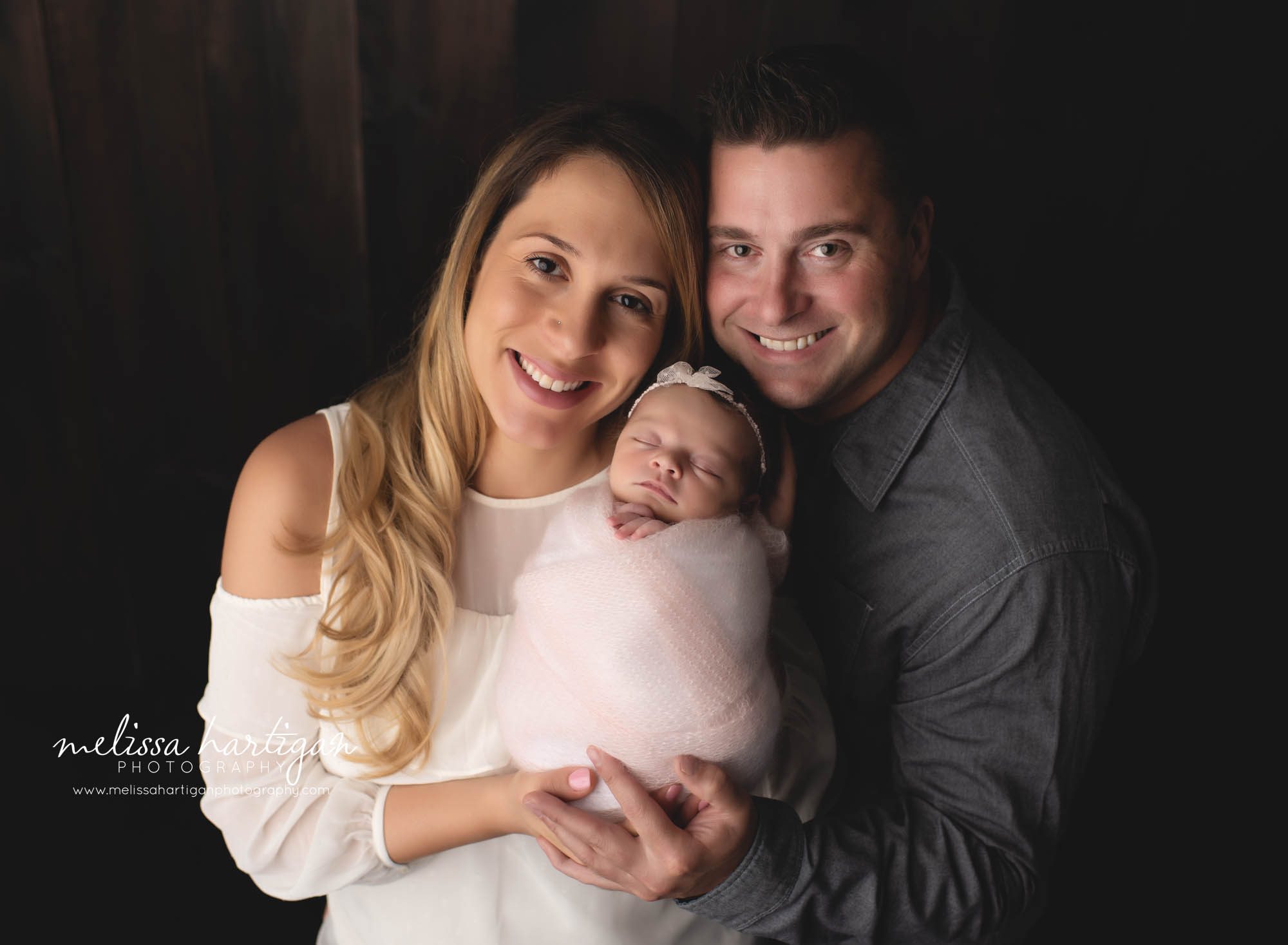 mom and dad holding newborn baby girl for first family photo in newborn photography studio session